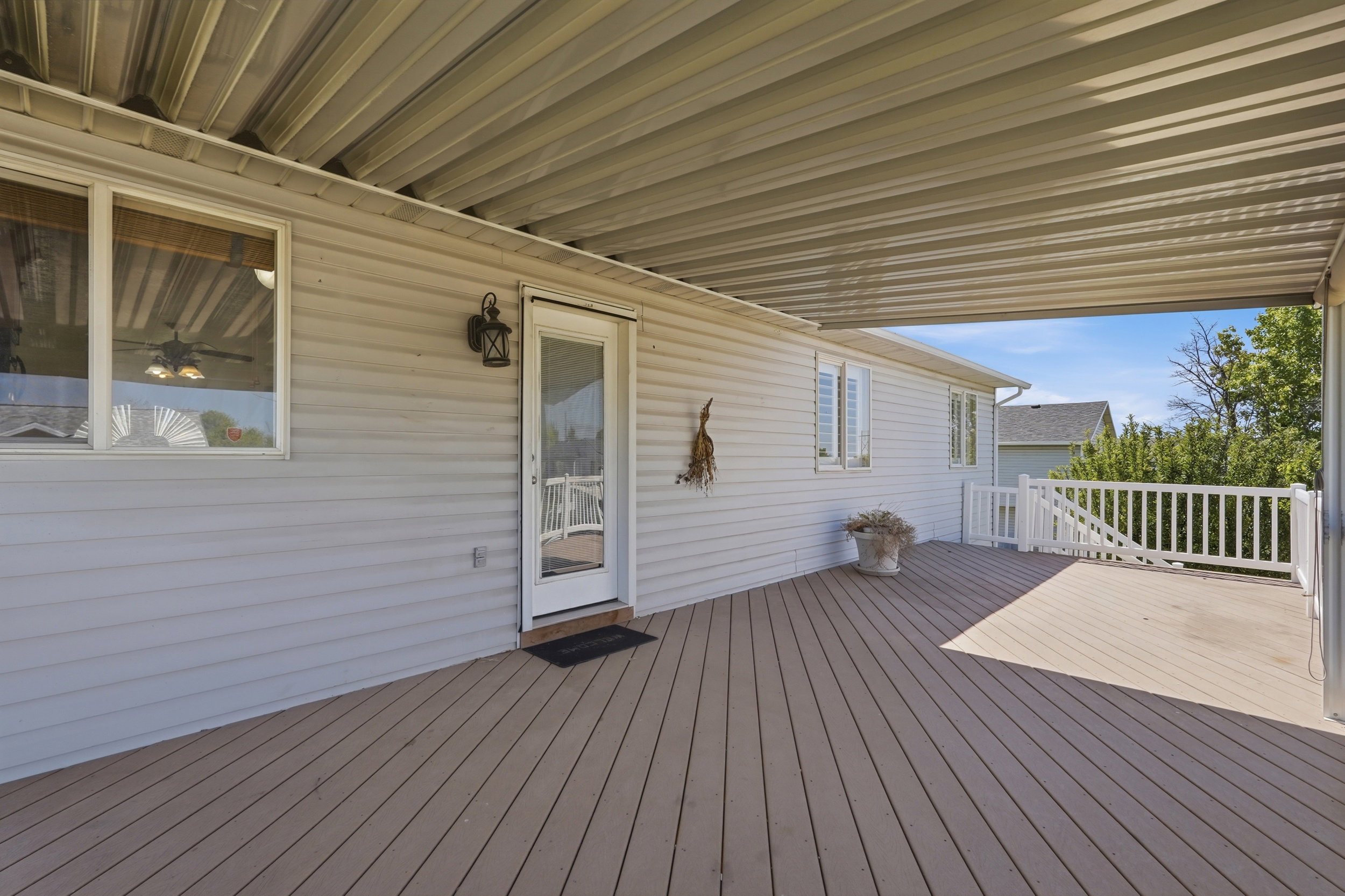Expansive covered deck featuring wood-finish flooring, white vinyl siding, and a white railing system