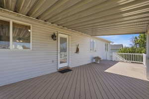 Expansive covered deck featuring wood-finish flooring, white vinyl siding, and a white railing system