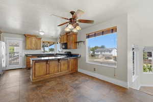 Kitchen featuring wood cabinetry, dark countertops, a central island, tiled flooring, and a ceiling fan with integrated lighting