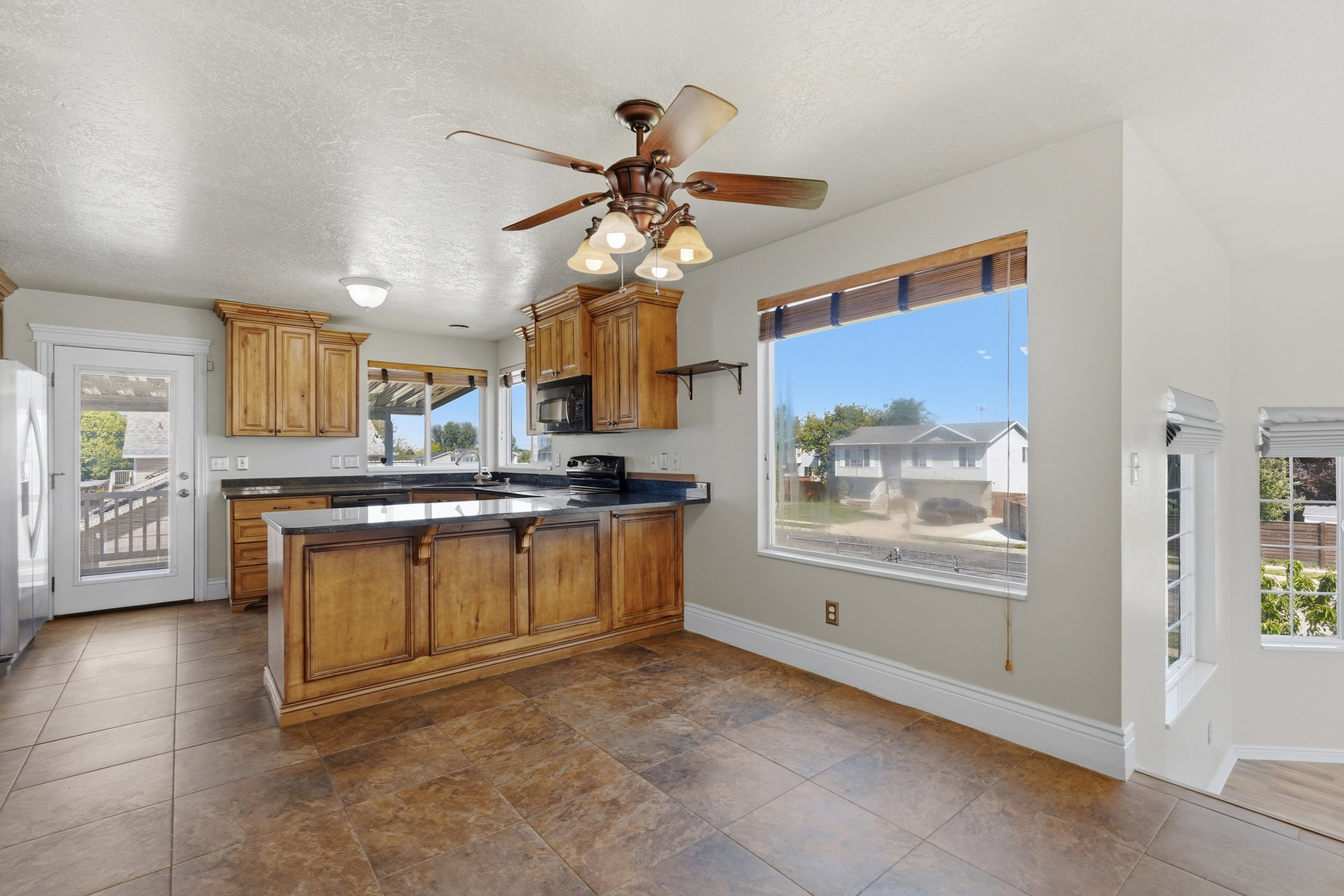 Kitchen featuring wood cabinetry, dark countertops, a central island, tiled flooring, and a ceiling fan with integrated lighting
