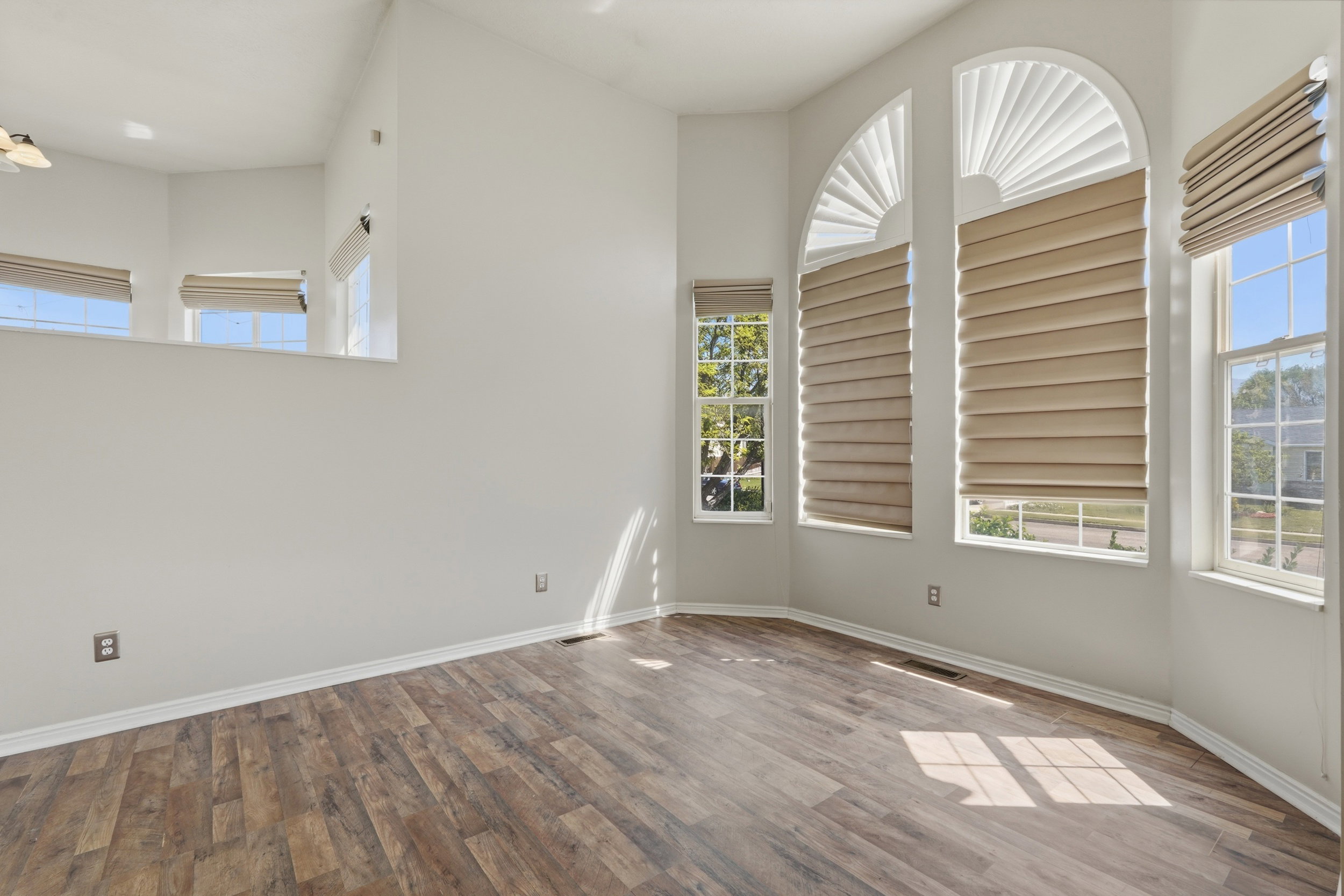 Vaulted ceiling interior featuring wood-finish flooring, multiple windows with blinds, and transom windows