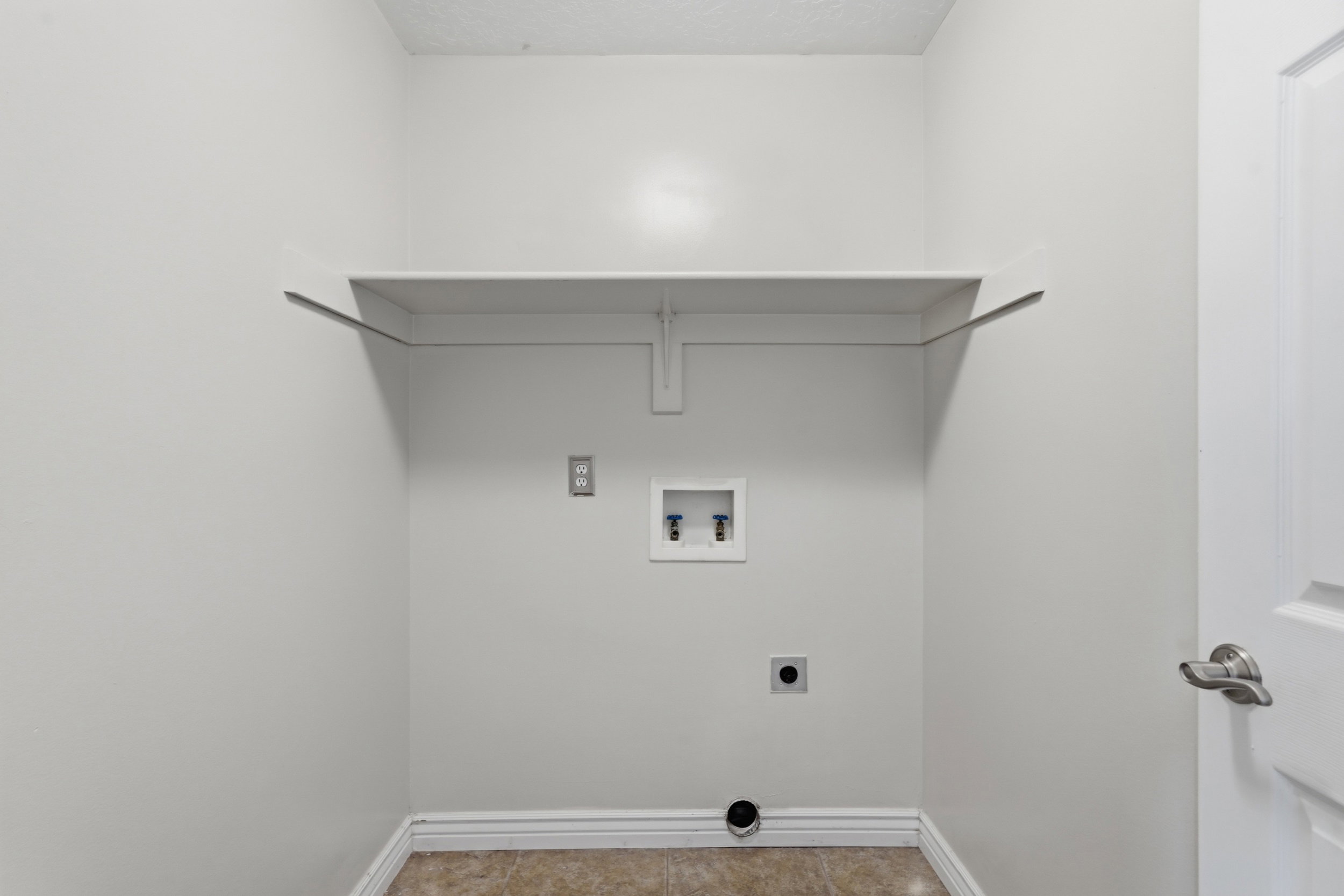 Dedicated laundry area featuring a built-in shelf, neutral wall tones, tile flooring, and a white paneled door with brushed nickel hardware