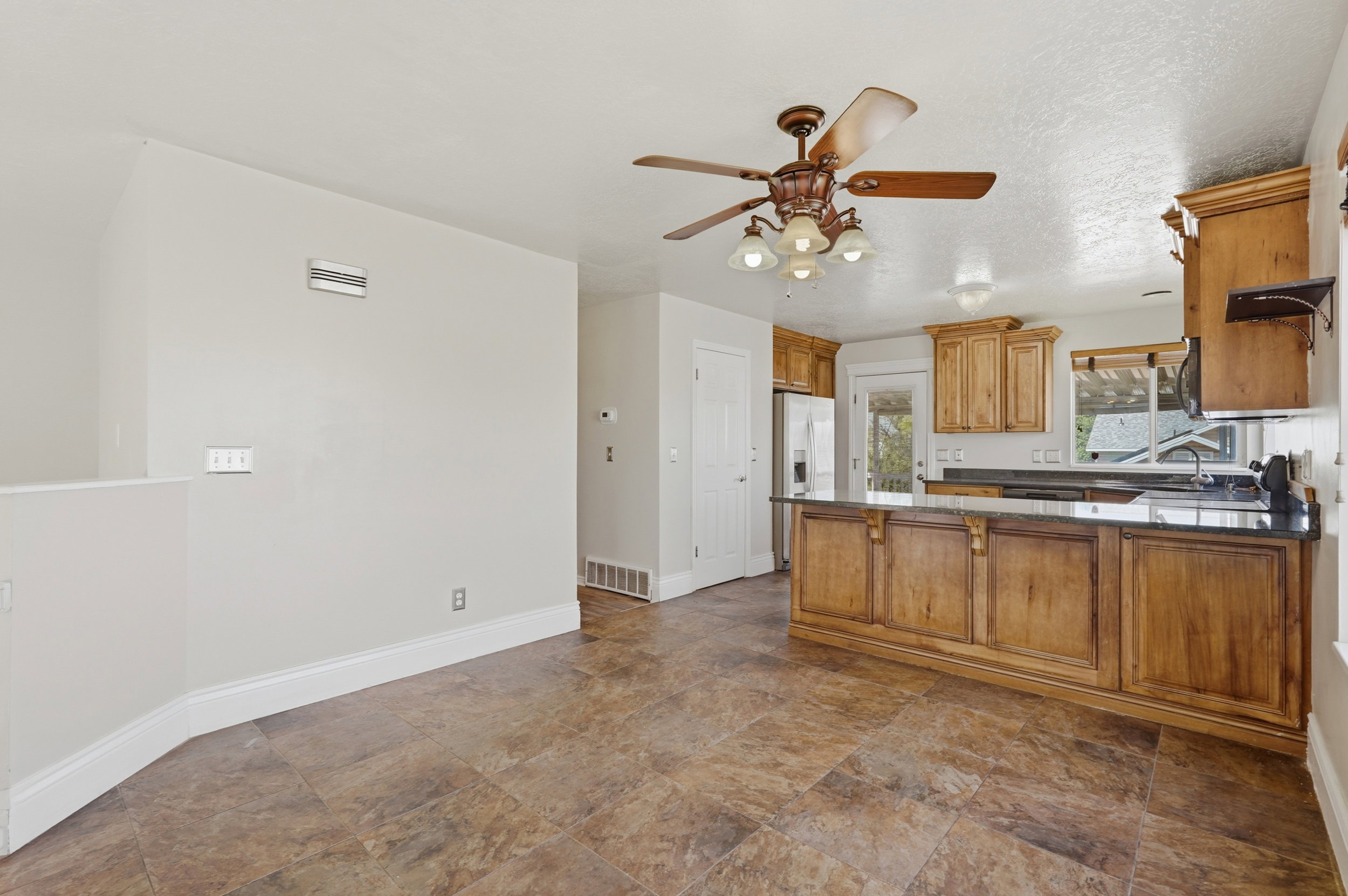 Spacious kitchen featuring wood cabinetry, black countertops, stainless steel appliances, and a central island with decorative detailing