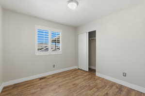 Neutral-toned room featuring a window with white shutters, wood-finish flooring, a built-in closet with bi-fold doors, and a ceiling-mounted light fixture
