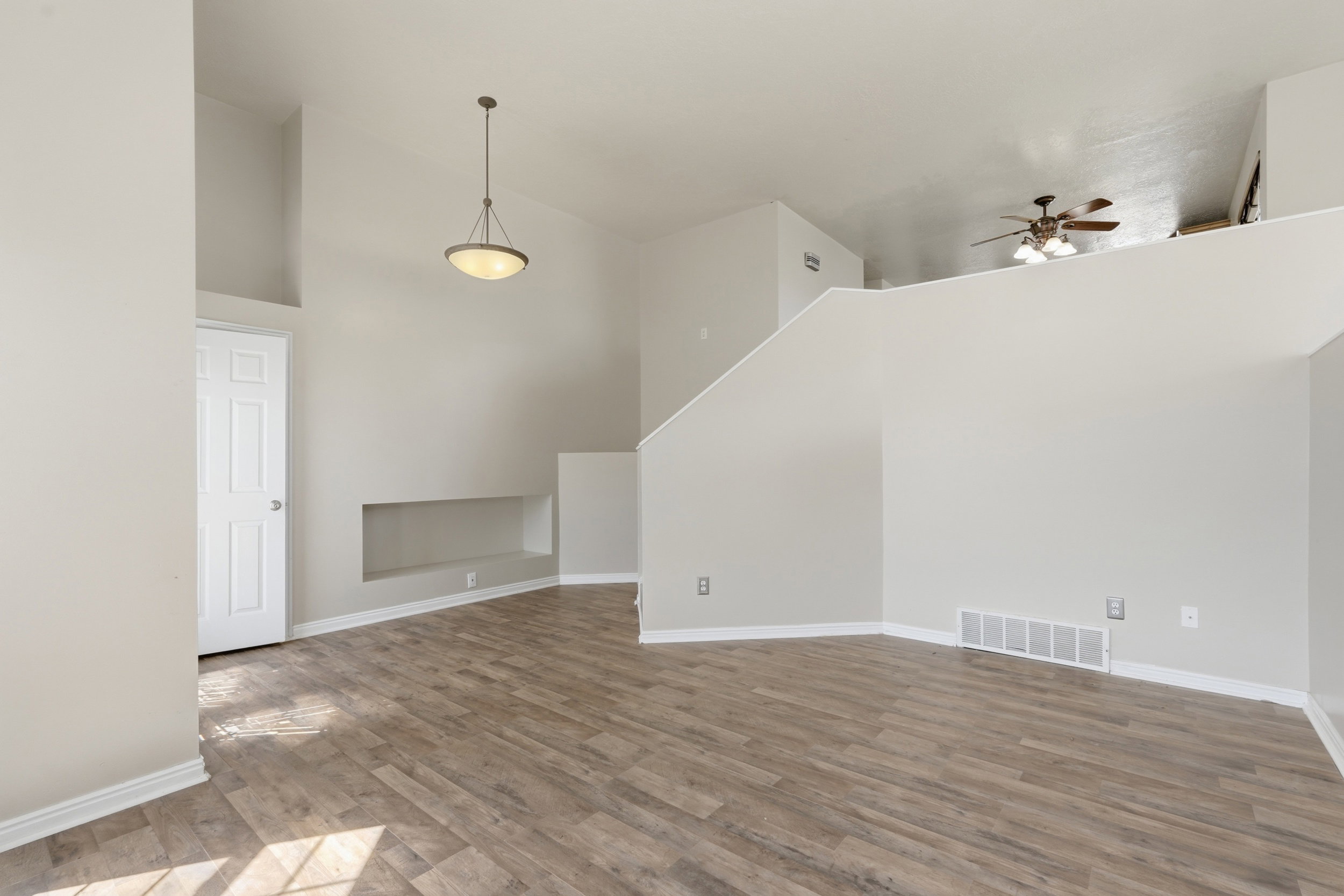 Vaulted ceiling living space featuring wood-finish flooring, a built-in wall niche, and a contemporary pendant light fixture