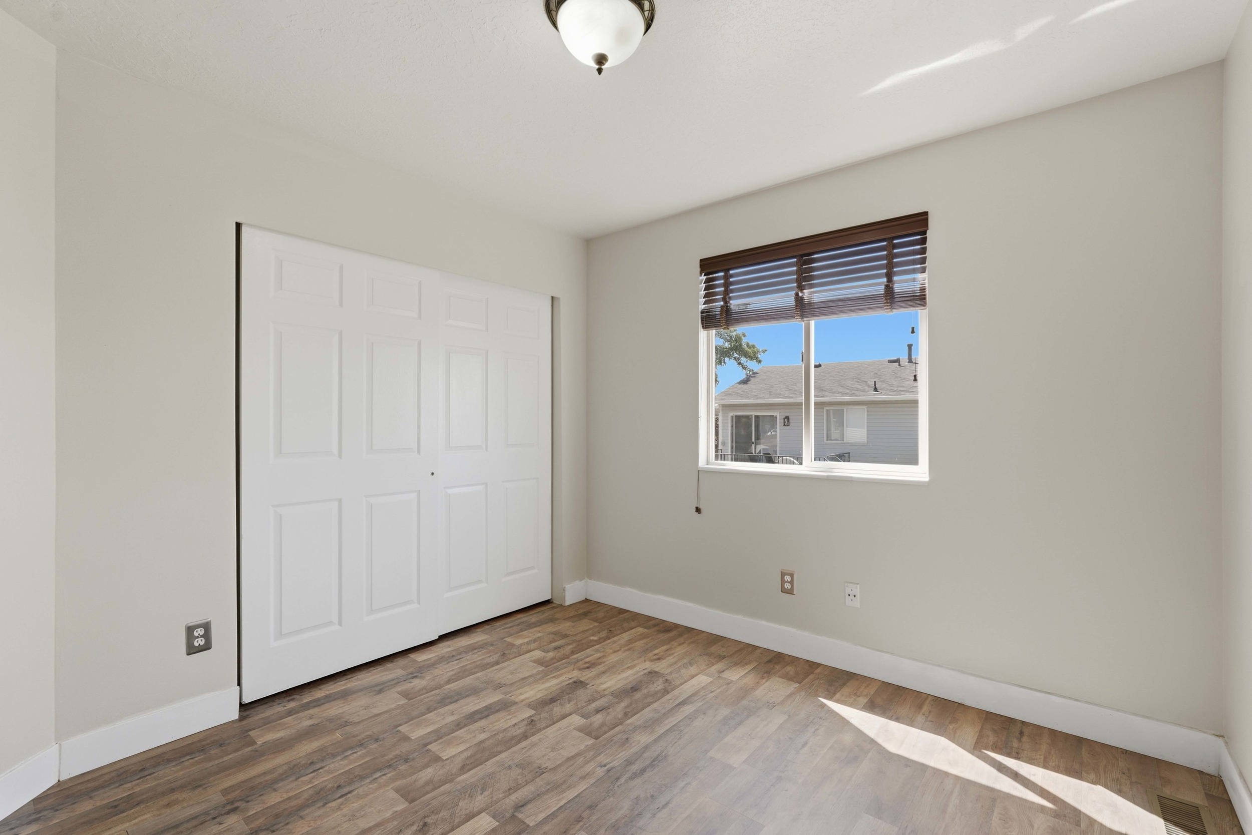 Neutral wall tones showcasing wood-finish flooring, a bi-fold closet, and a single window with horizontal blinds