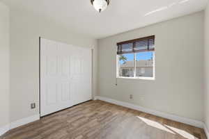 Neutral wall tones showcasing wood-finish flooring, a bi-fold closet, and a single window with horizontal blinds