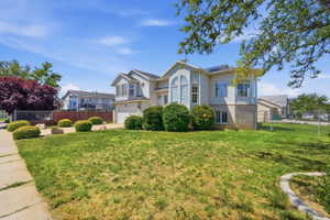 Two-story stucco and stone exterior featuring an arched window, bay window, attached two-car garage, and established front landscaping