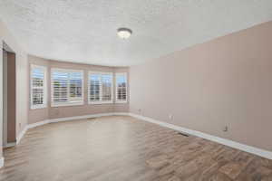 Expansive room featuring multiple windows with plantation shutters, wood-finish flooring, neutral wall tones, white baseboards, and a flush-mount ceiling light fixture