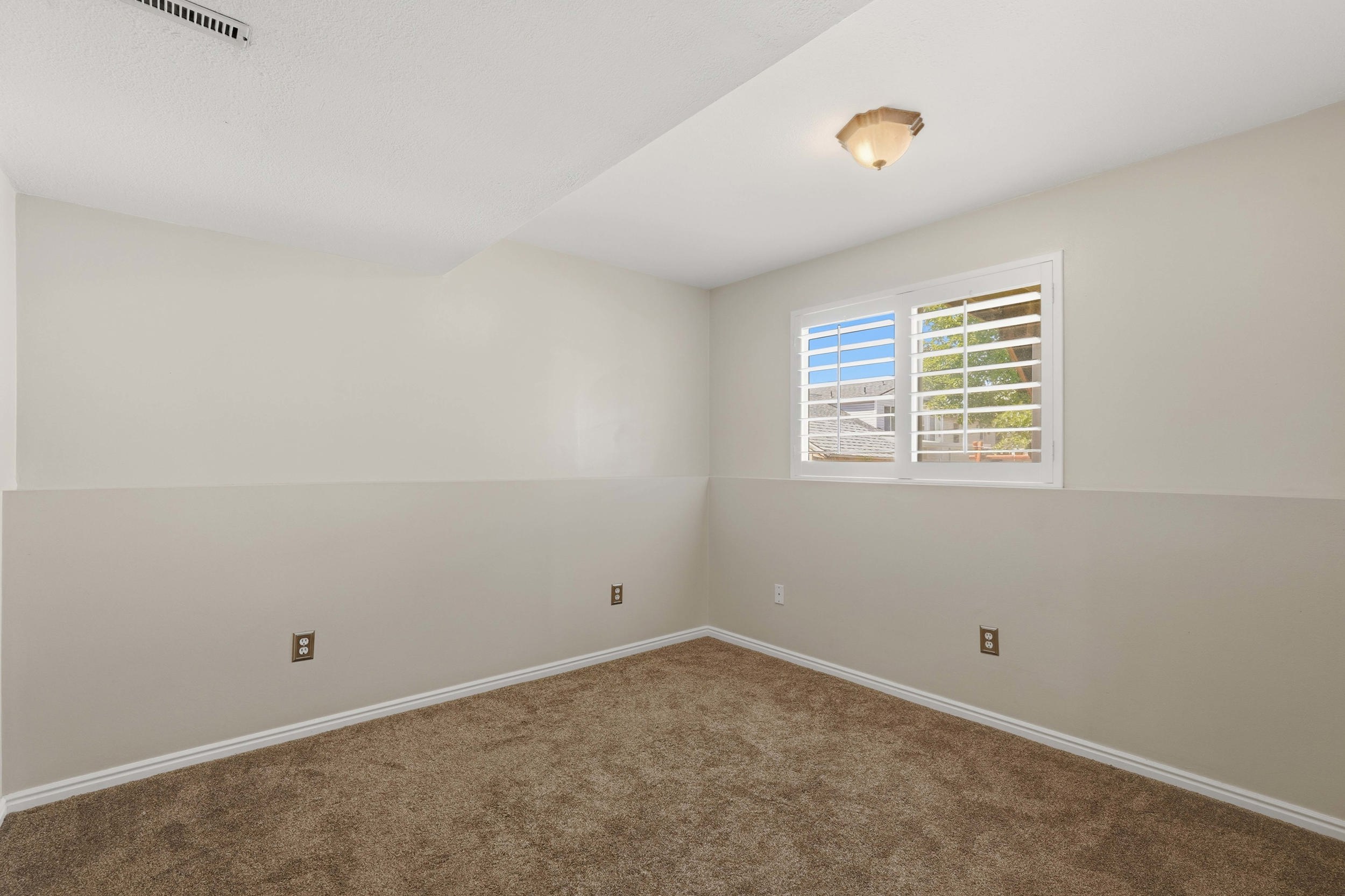 Room featuring neutral two-tone wall paint, a window with white louvered blinds, and brown carpet flooring