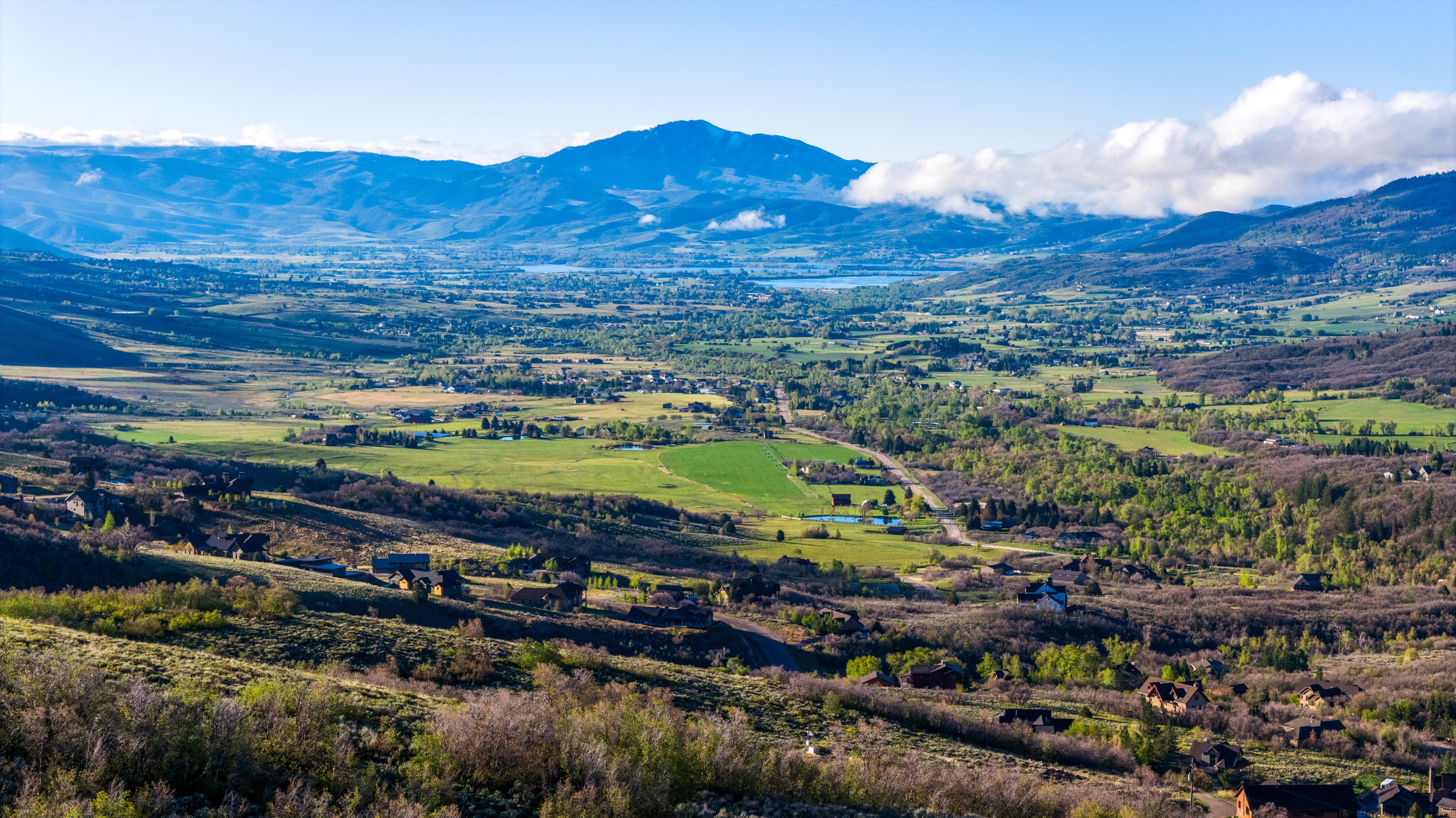 Expansive valley with varied terrain, featuring distant mountains, a discernible body of water, and scattered residential properties