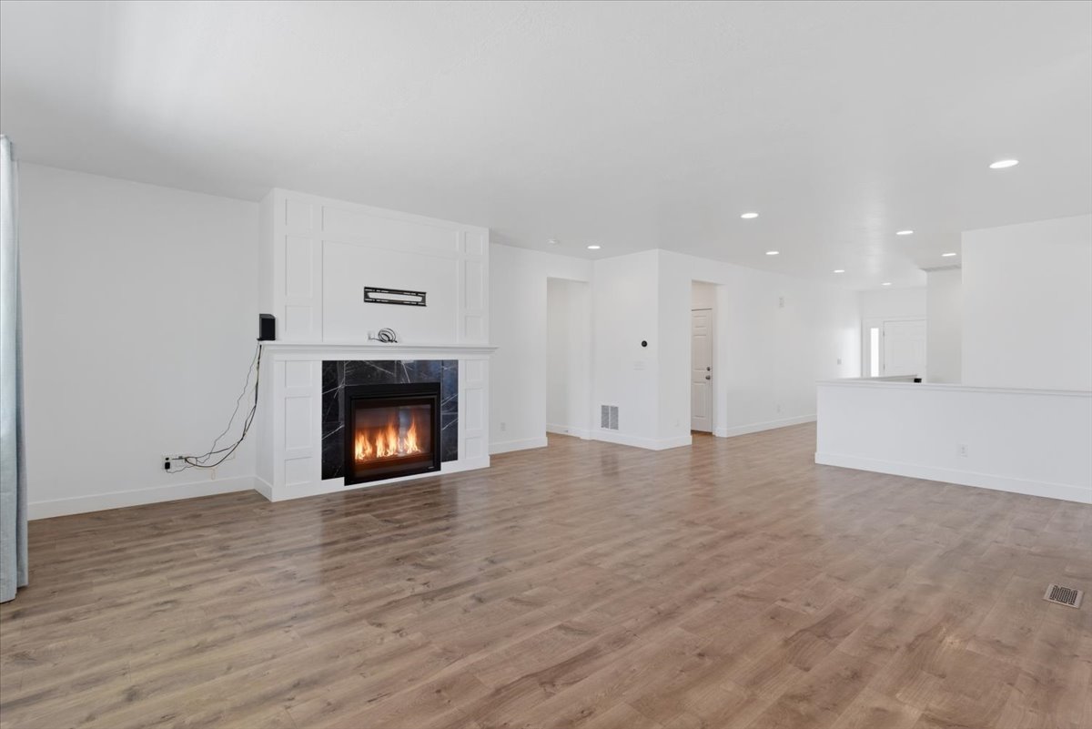 Spacious interior featuring wood-finish flooring, recessed lighting, and a contemporary fireplace with a white mantel and dark stone surround