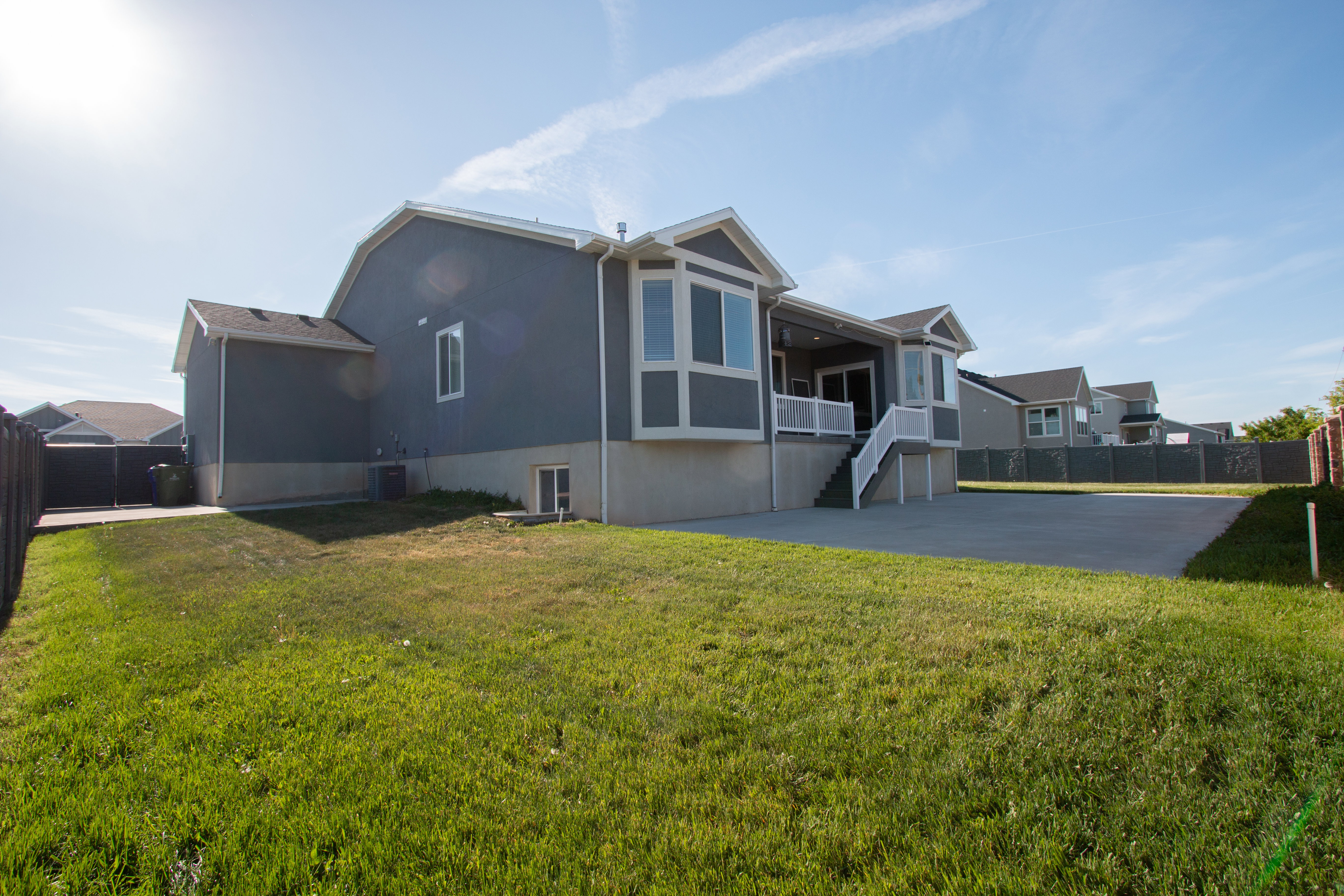 Expansive backyard featuring a large concrete patio, manicured lawn, and a multi-level house with a deck and bay windows
