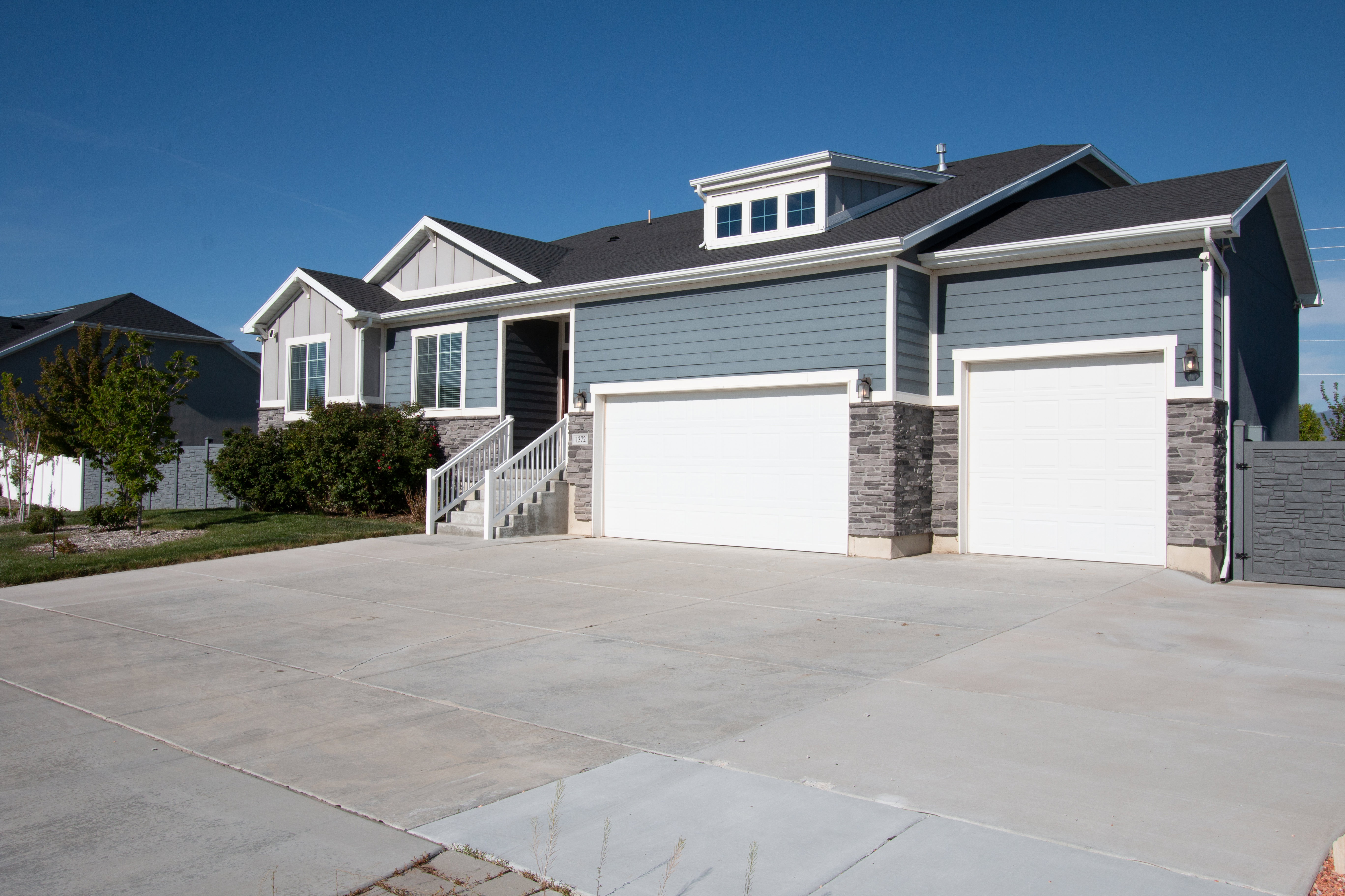 Contemporary exterior with blue and gray siding, stone accents, two-car garage, dormer window, and mature landscaping