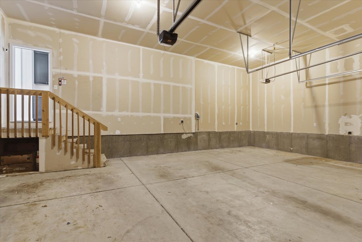Spacious garage featuring a concrete floor, exposed drywall walls, and a wood-finished staircase with a railing
