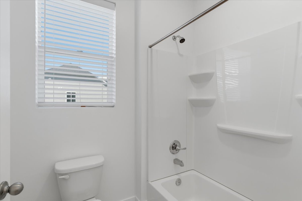 White bathroom featuring a shower-tub combination, chrome fixtures, and a window with horizontal blinds