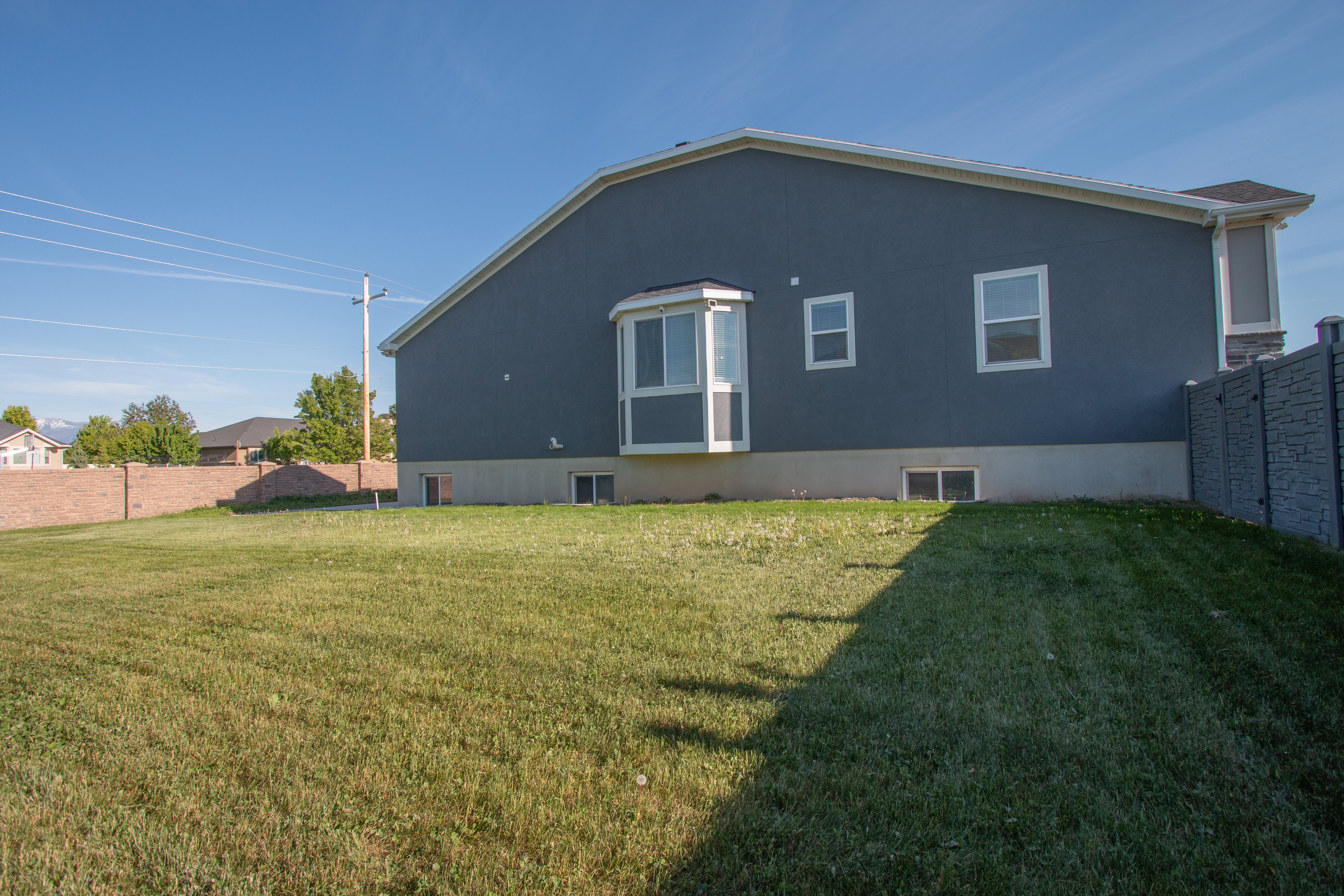 Expansive green lawn bordering the property, featuring a stucco exterior with a bay window and multiple white-framed windows