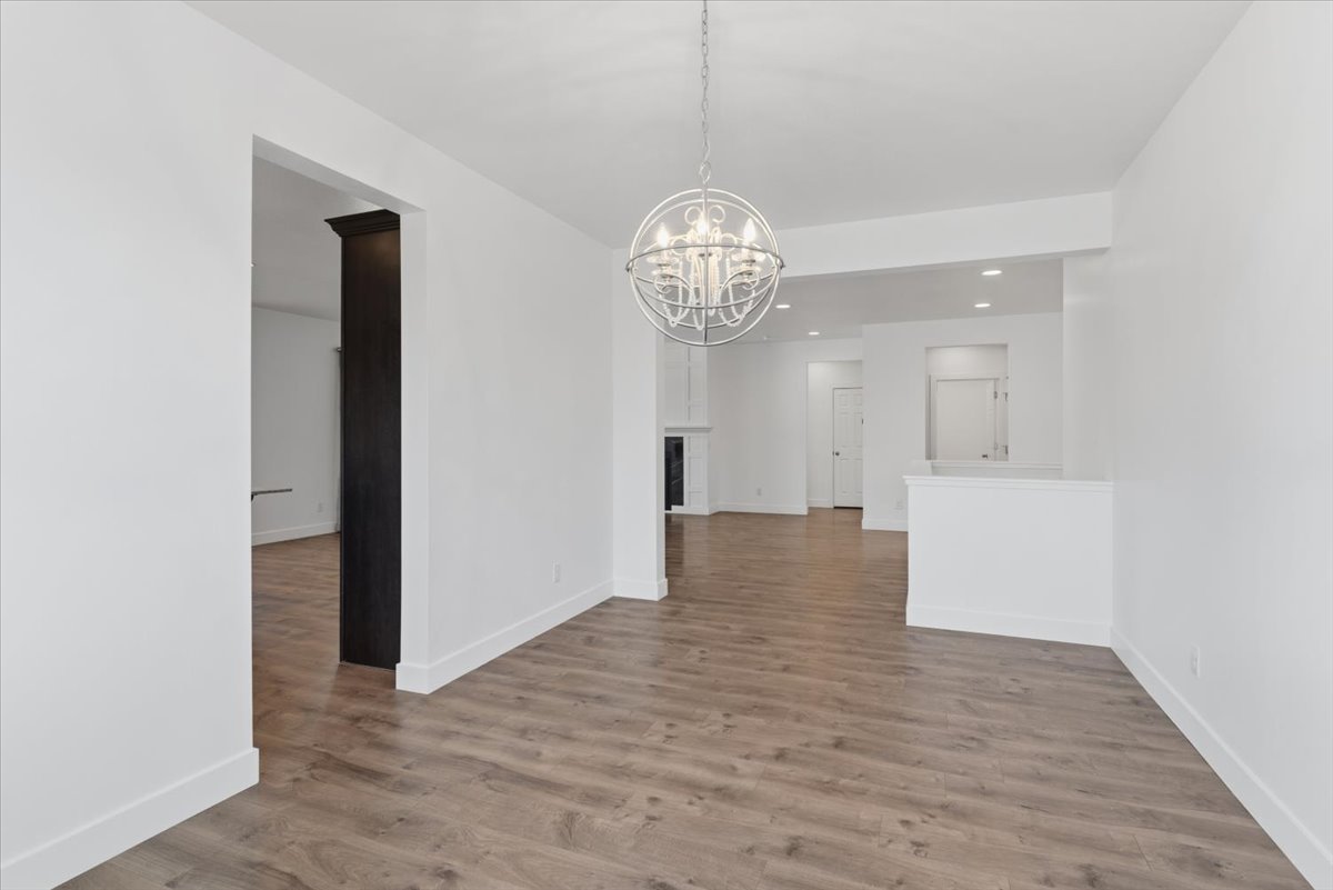 Open-concept living area featuring wood-finish flooring, white walls, and a contemporary spherical chandelier