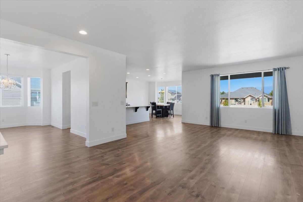 Spacious living area featuring wood-finish flooring, recessed lighting, and a large window with blue drapes