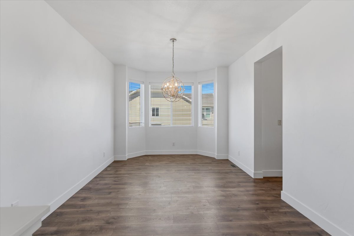 Spacious room featuring a bay window, wood-finish flooring, white baseboards, a contemporary spherical chandelier, and an open doorway