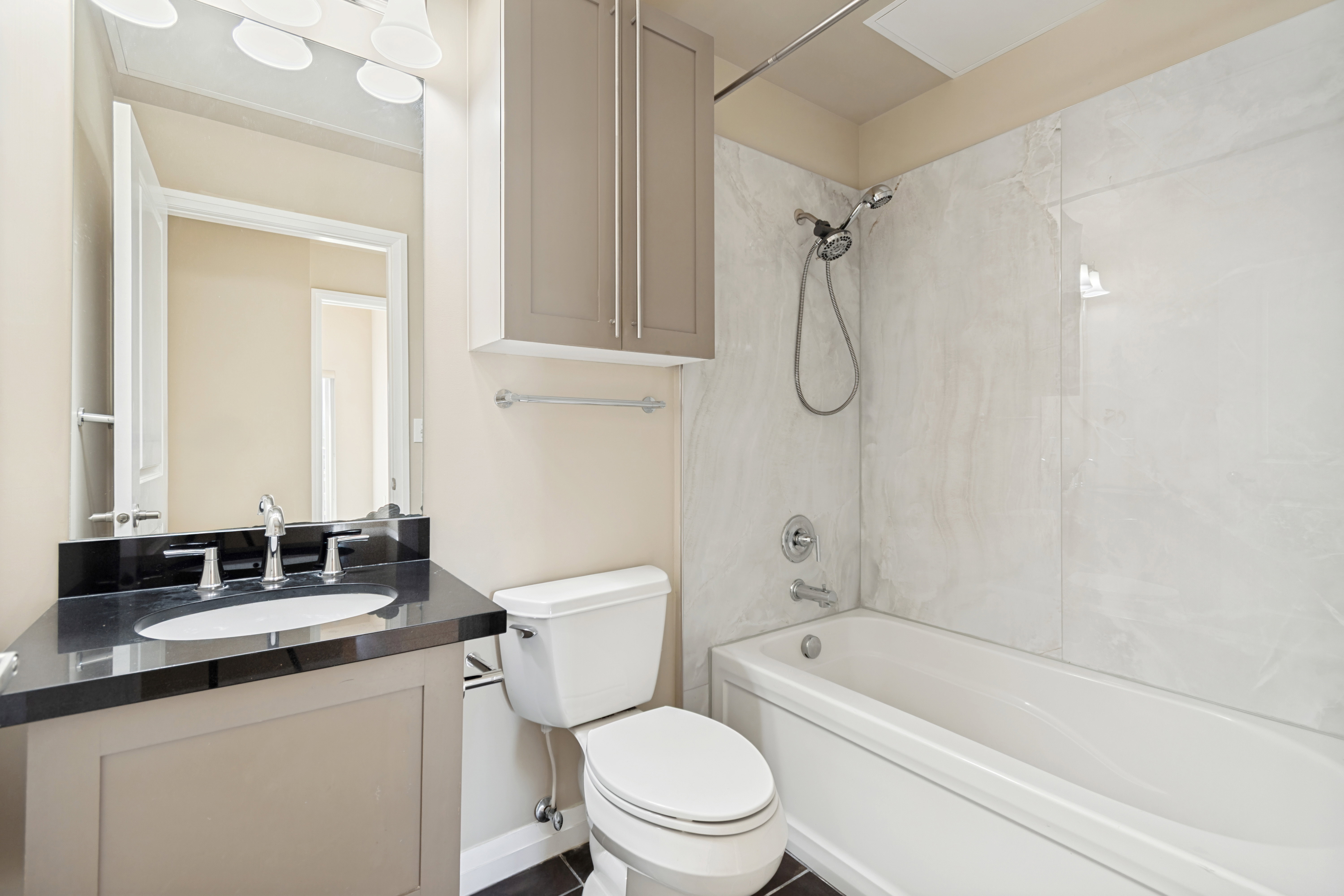Bathroom featuring a built-in tub with a shower fixture, light-toned wall panels, and a vanity with a dark countertop
