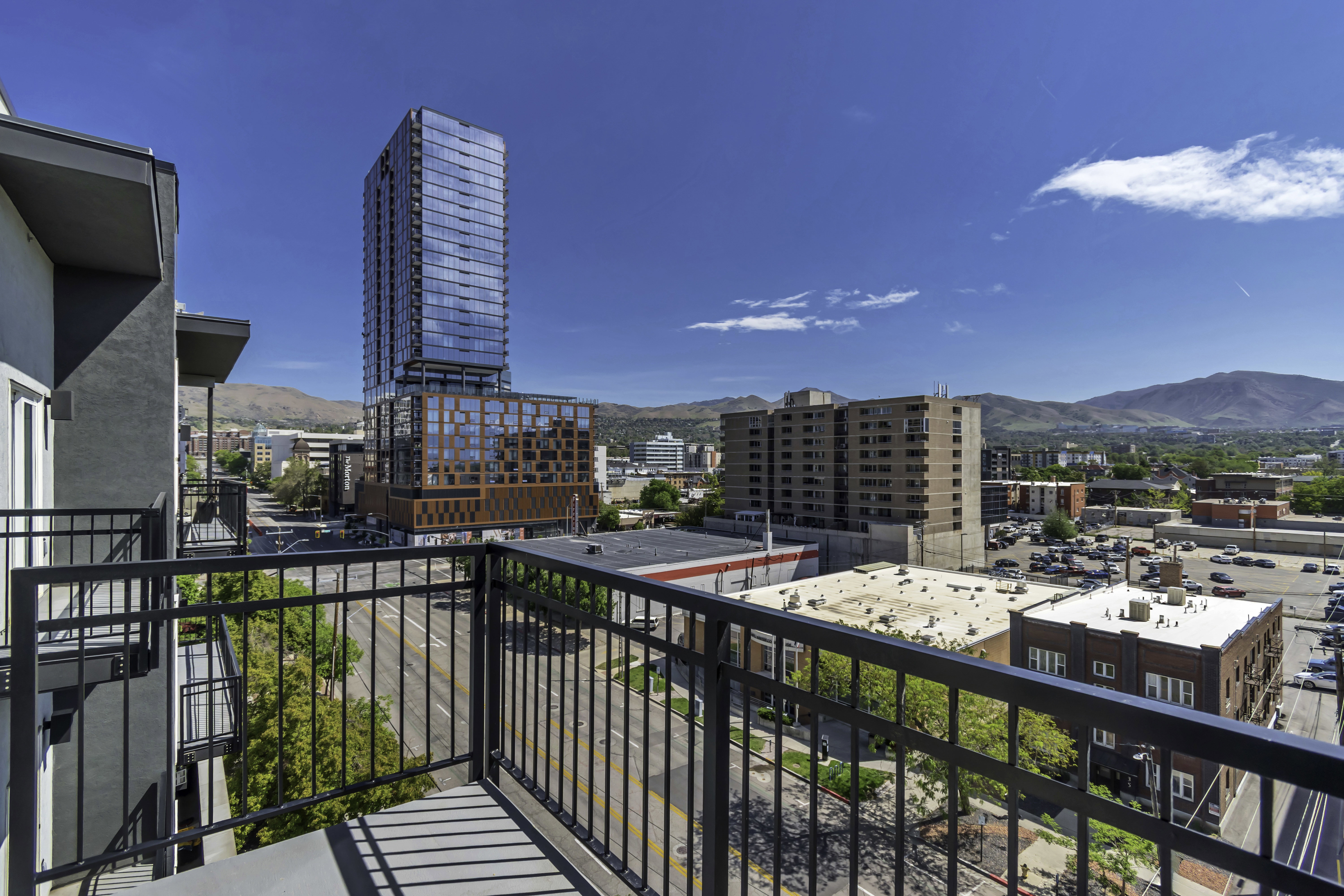 Private balcony with black metal railing, overlooking urban streetscape and distant mountains