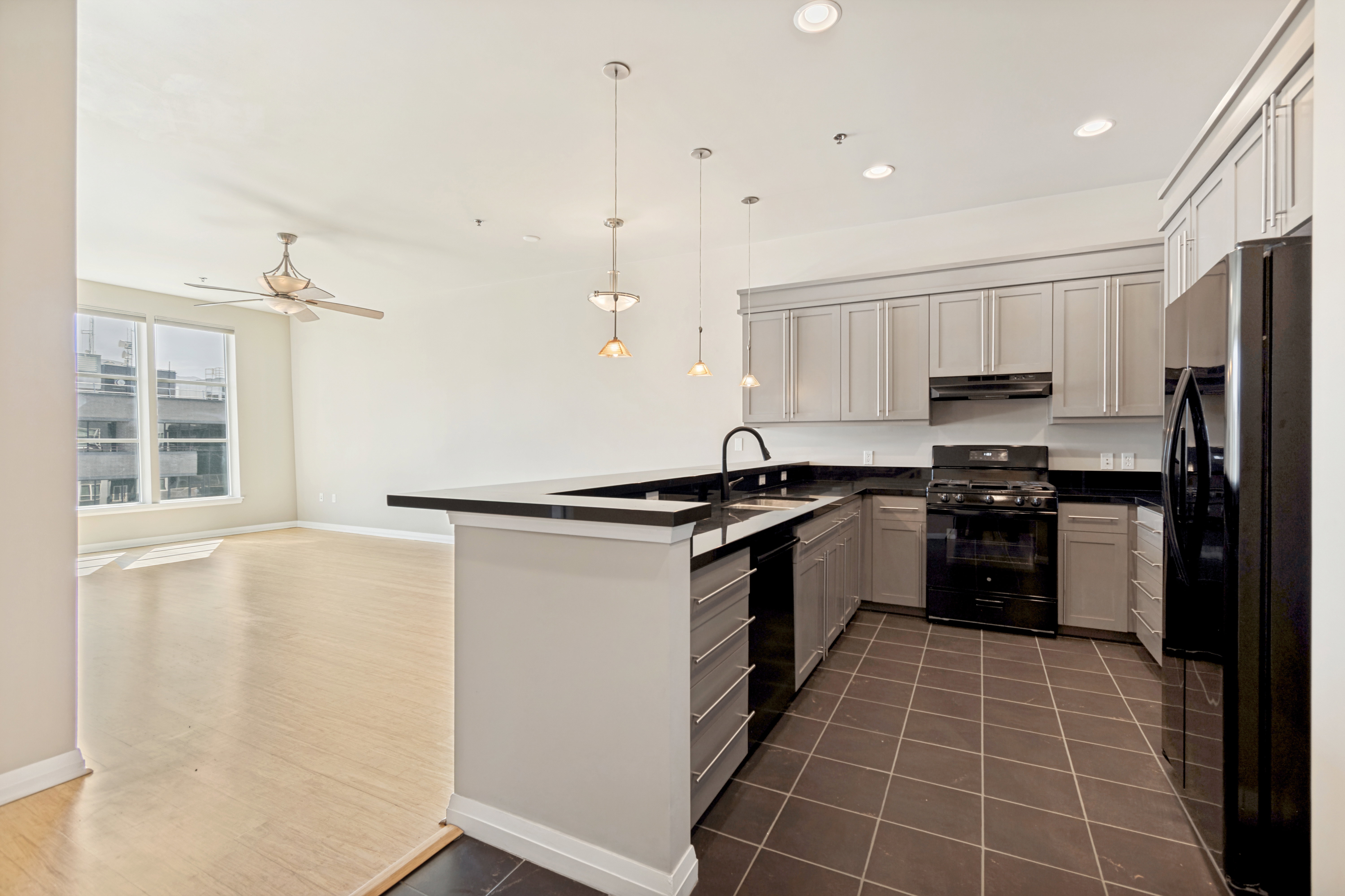 Kitchen with dark tile flooring, gray cabinetry, black appliances, and dark countertops, featuring a breakfast bar with pendant lighting