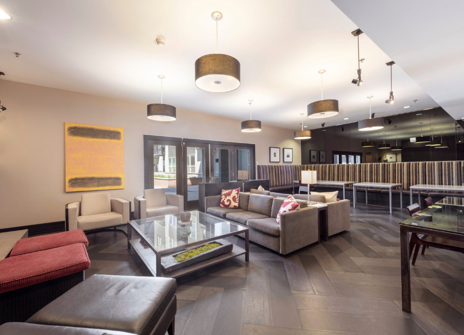 Spacious common area featuring dark wood-finish flooring in a herringbone pattern, multiple seating arrangements, recessed lighting, and drum pendant fixtures