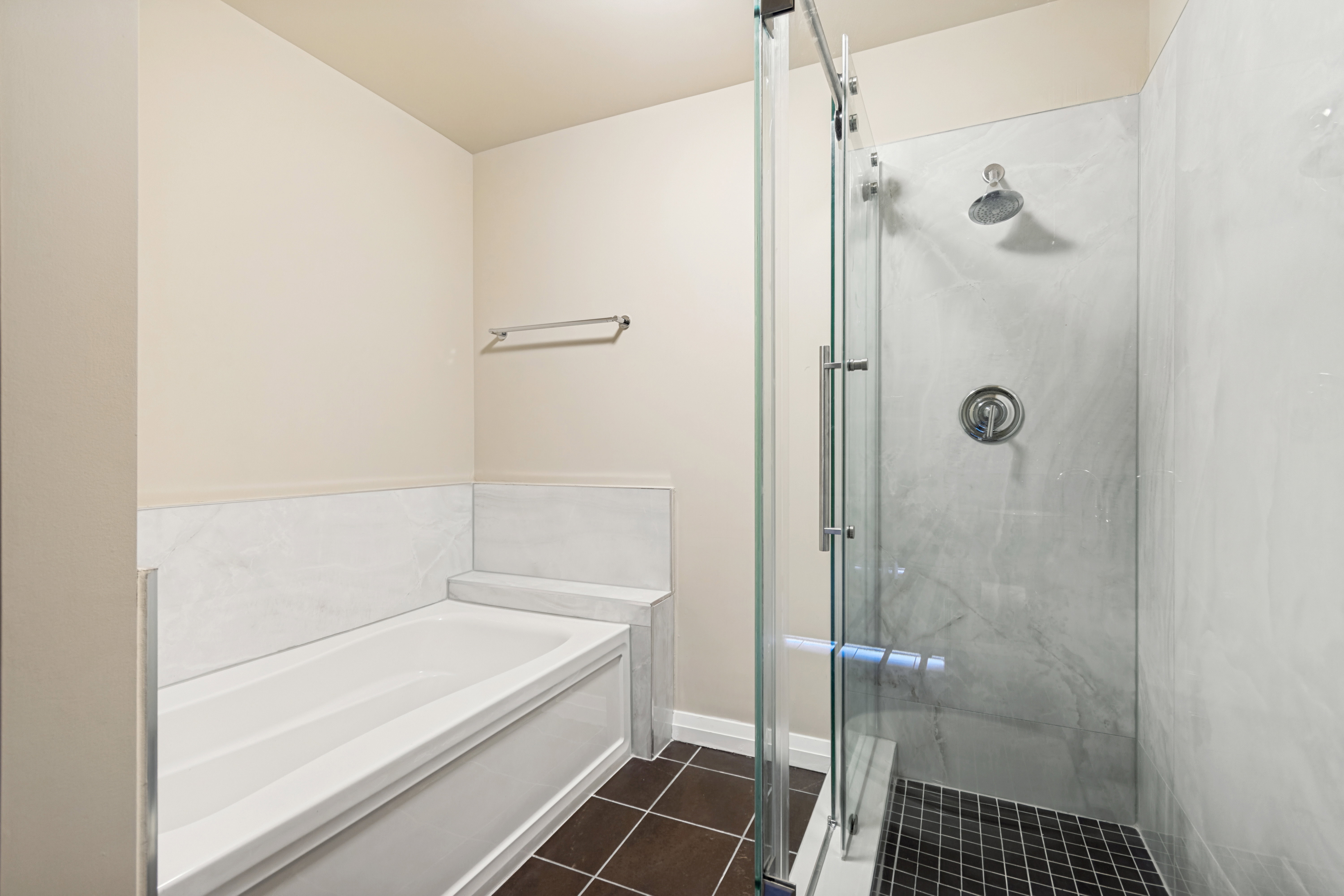 Glass-enclosed shower with a rainfall showerhead, white marble-style wall panels, and dark square floor tiles