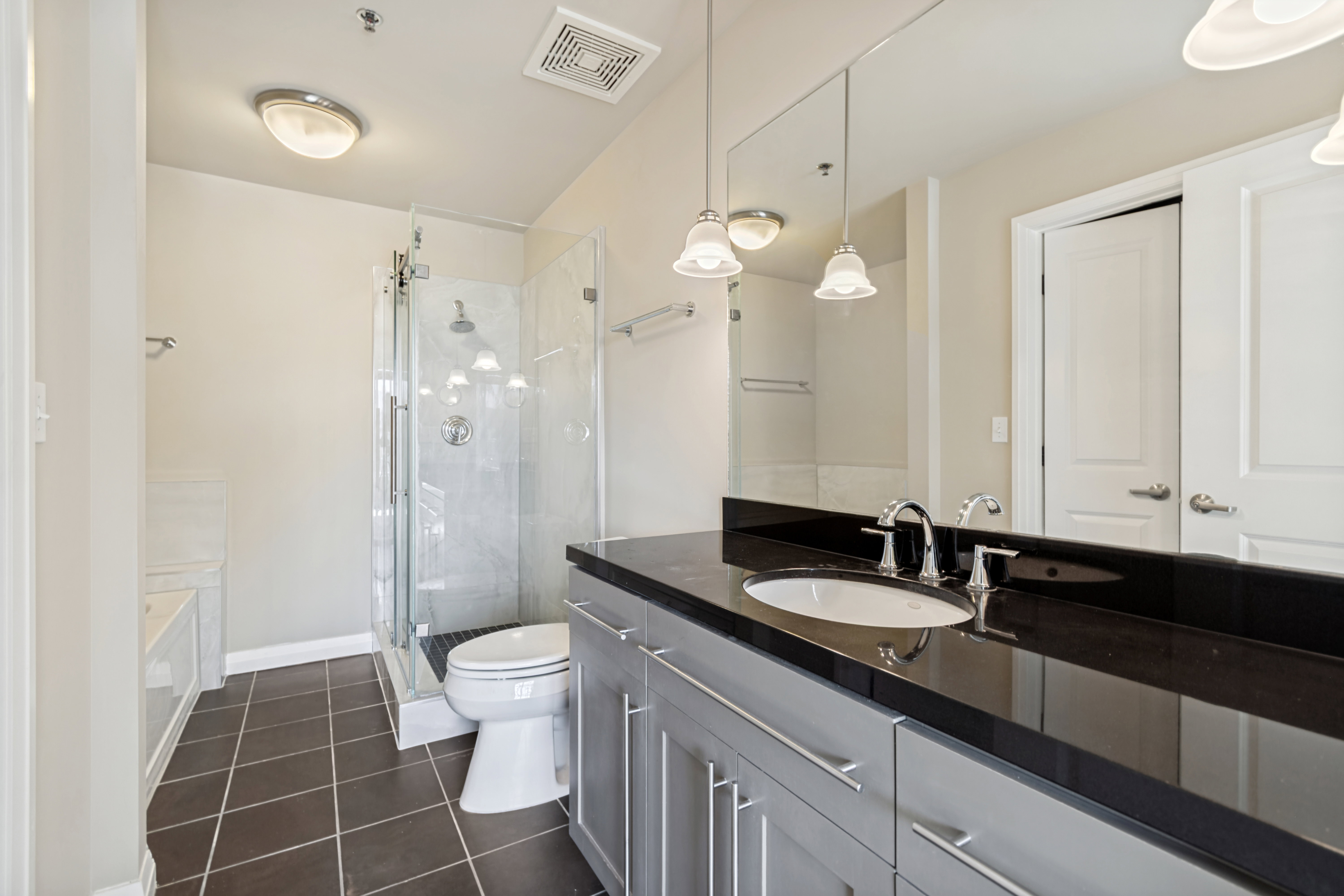 Master Bathroom featuring a double vanity with a dark countertop and pendant lighting, a glass-enclosed shower, and a separate soaking tub