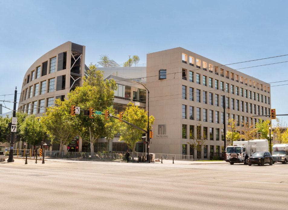 Modern library across the street featuring a curved facade, extensive window arrays, structured rooftop elements, and a light-toned exterior