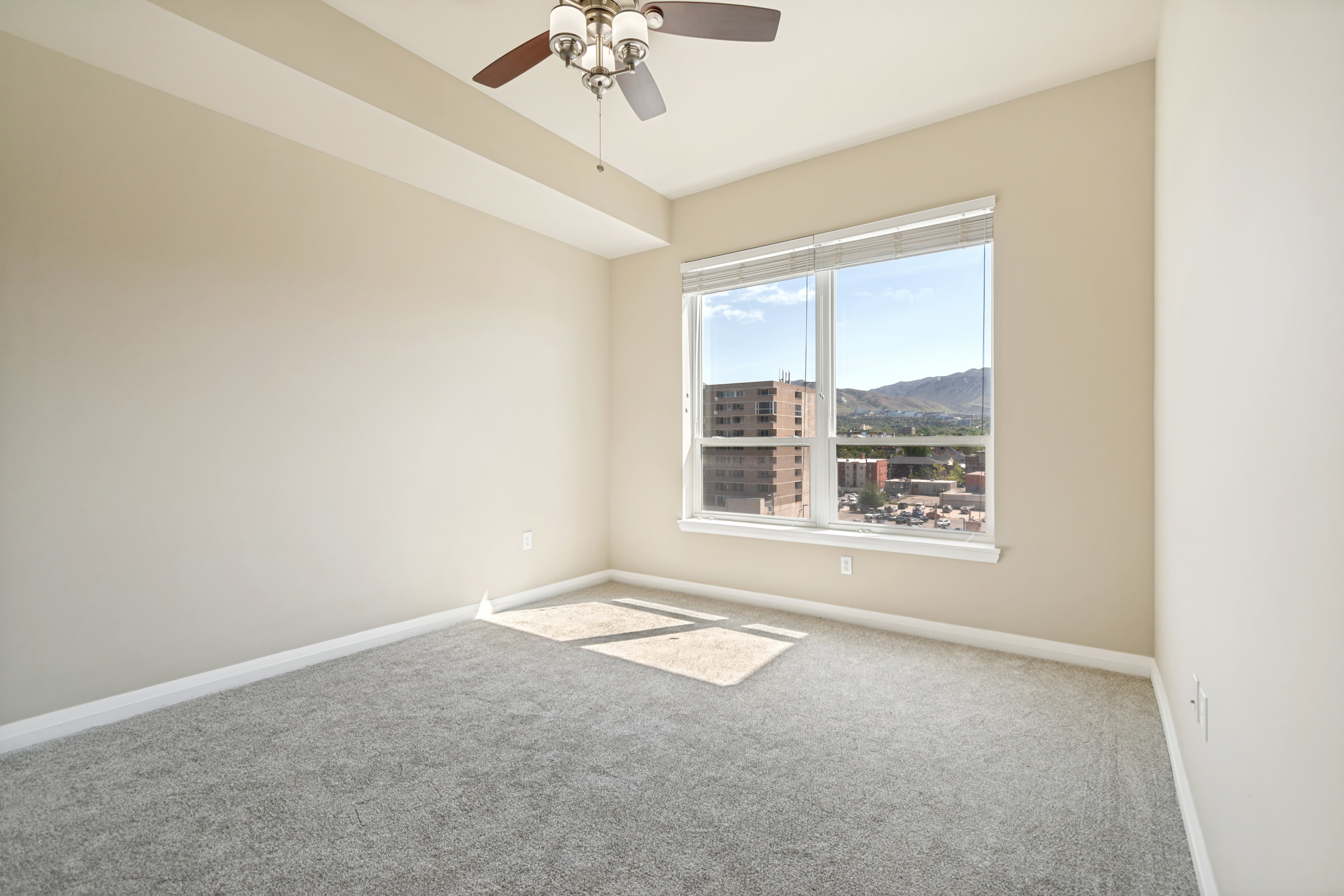 Neutral-toned room featuring a large window, light-colored walls, and gray carpeting