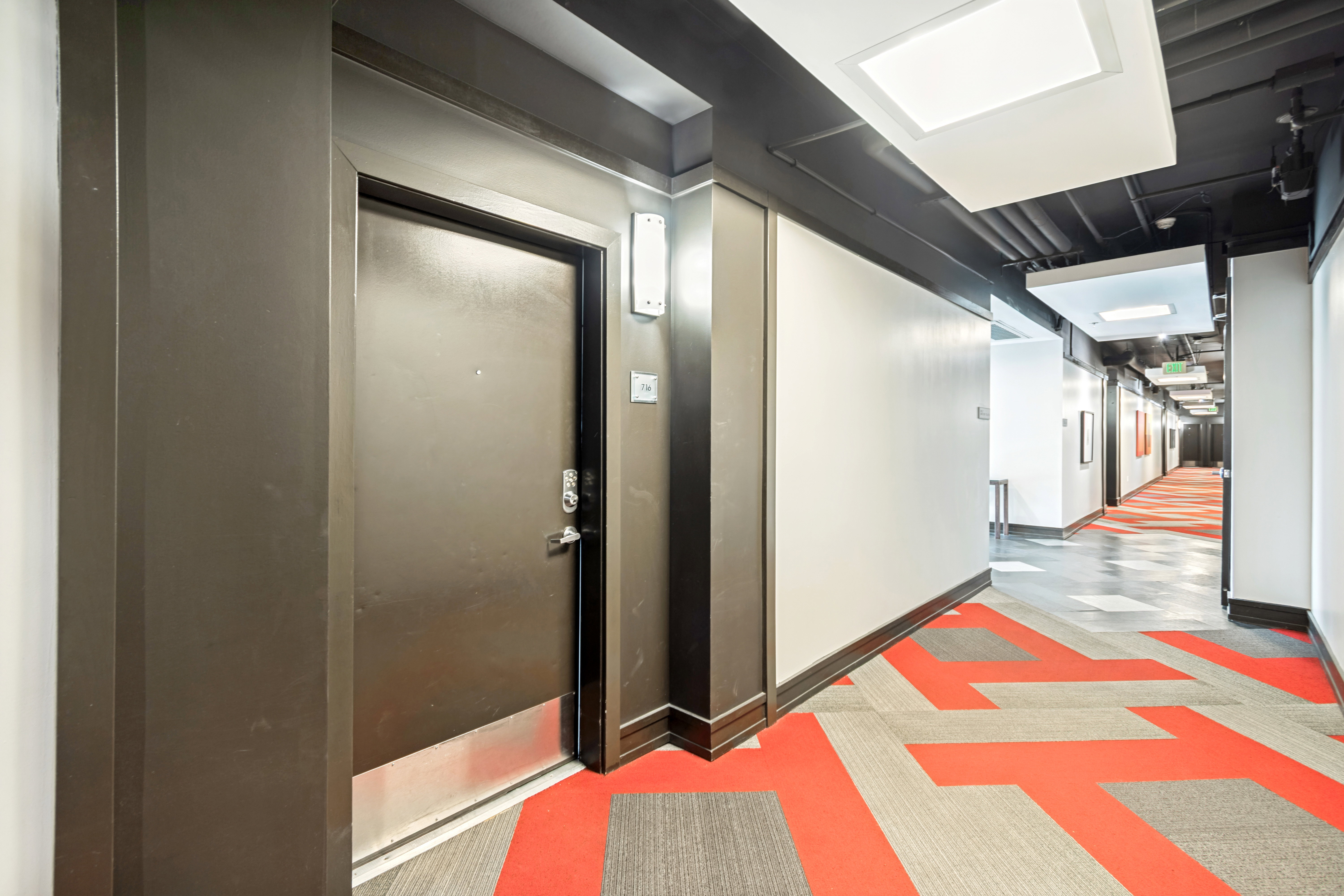 Hallway entrance featuring a dark-toned door with a security viewer and brushed metal kickplate