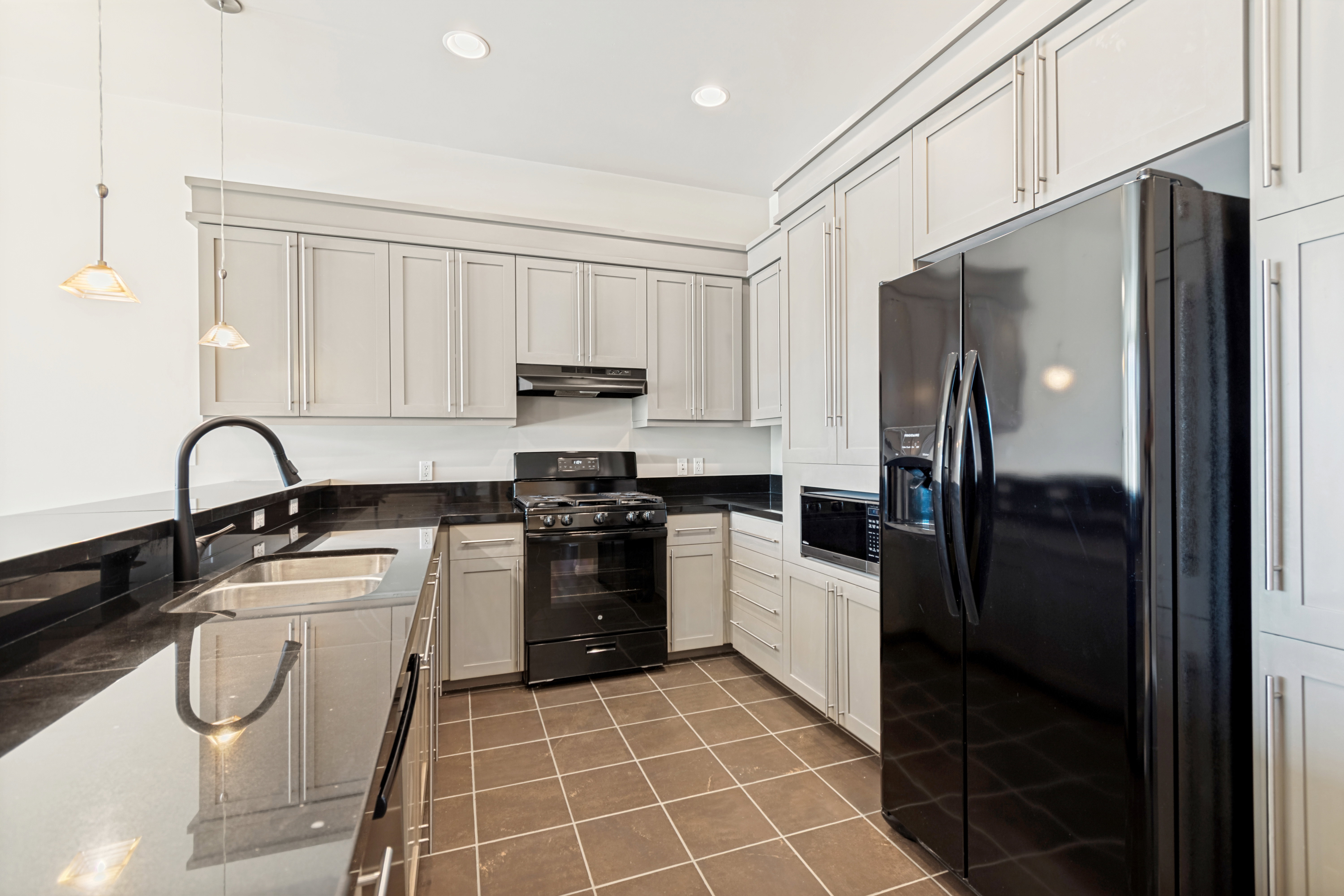 Modern kitchen featuring black appliances, light-toned cabinetry, dark countertops, a double basin sink with a gooseneck faucet, and pendant lighting