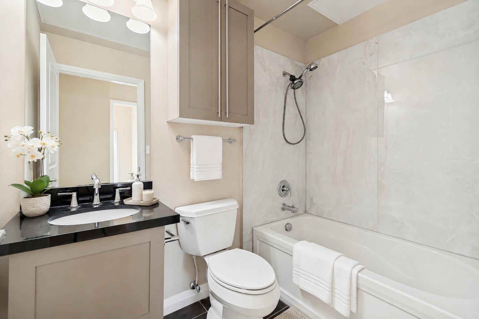 Bathroom featuring a single vanity with a black countertop and an undermount sink, a wall-mounted medicine cabinet, a toilet, a bathtub with a shower, and tiled shower walls