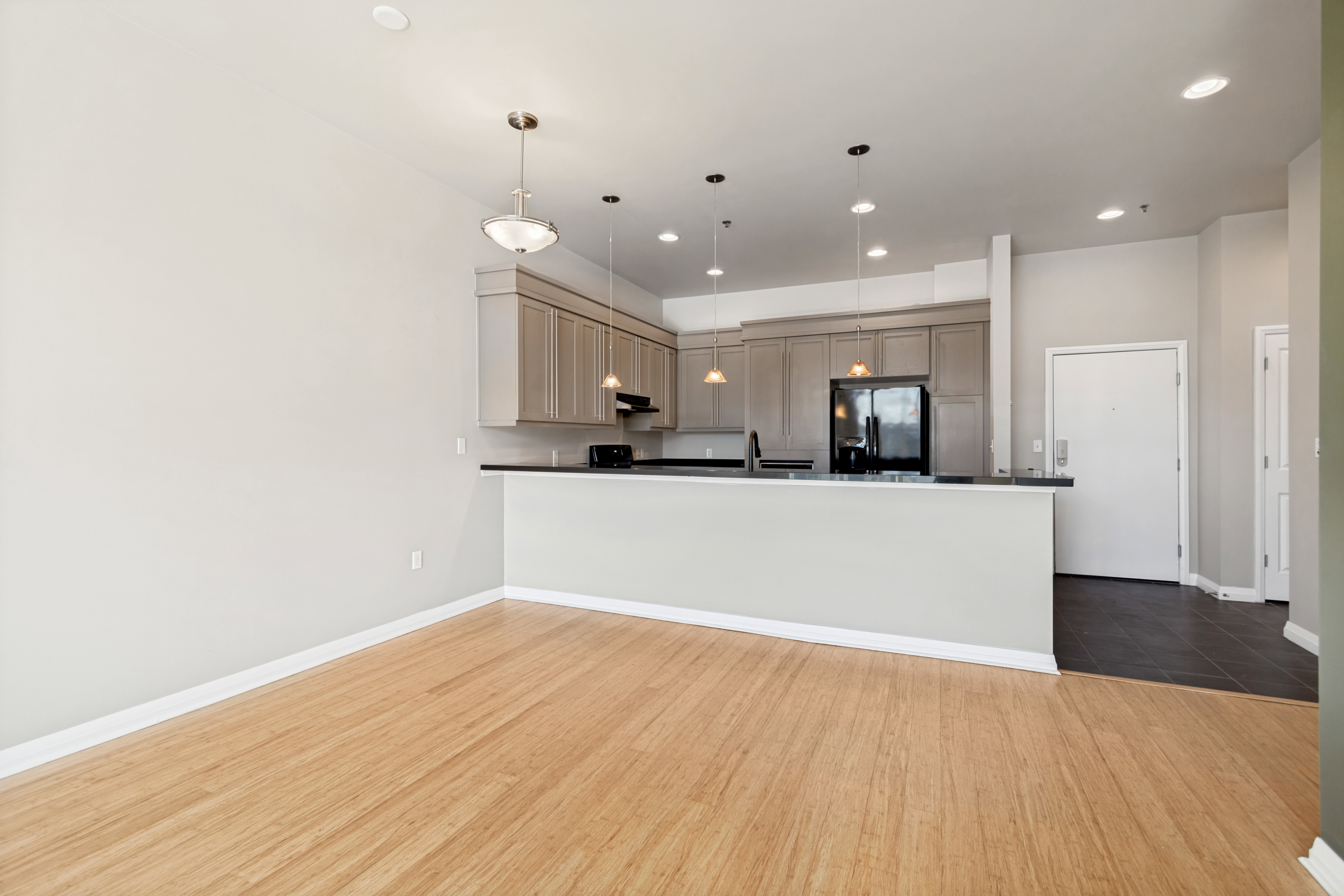 Open-concept living area featuring wood-finish flooring, a kitchen with grey cabinetry, dark countertops, and recessed lighting
