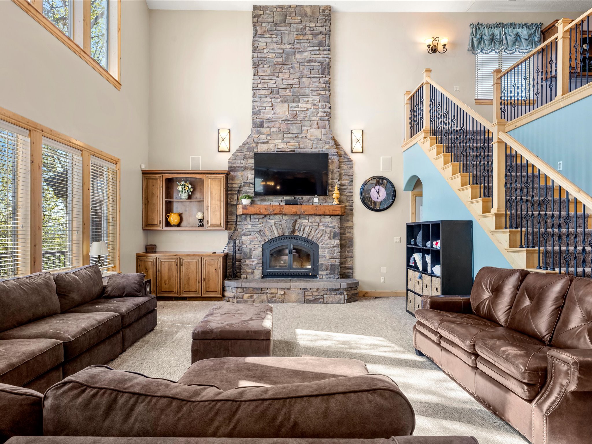 Vaulted living area featuring a stone-clad fireplace with wood mantle, built-in wood cabinetry, and extensive window-line