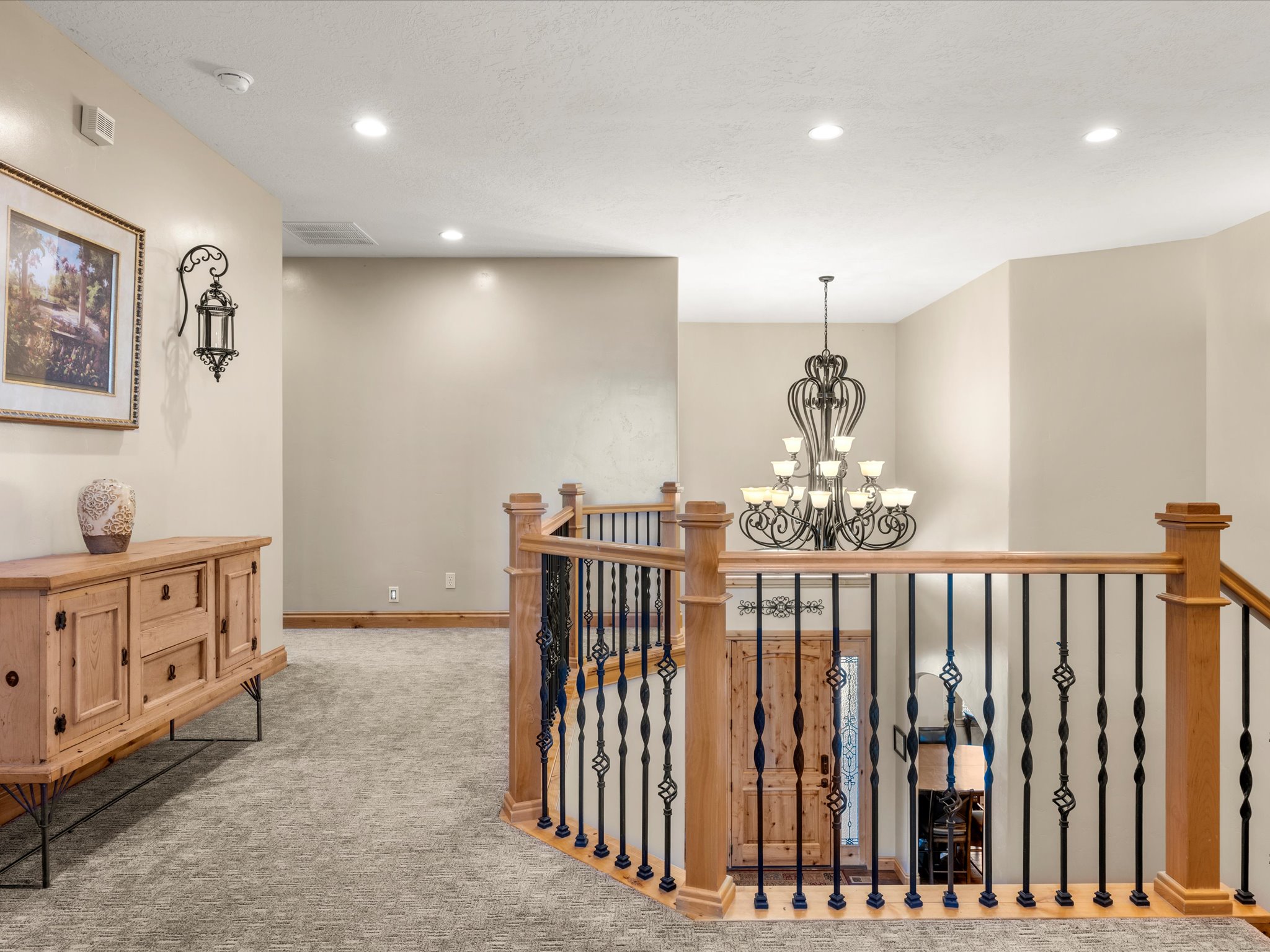 Carpeted hallway featuring a built-in wall sconce, recessed lighting, and a substantial wrought iron chandelier