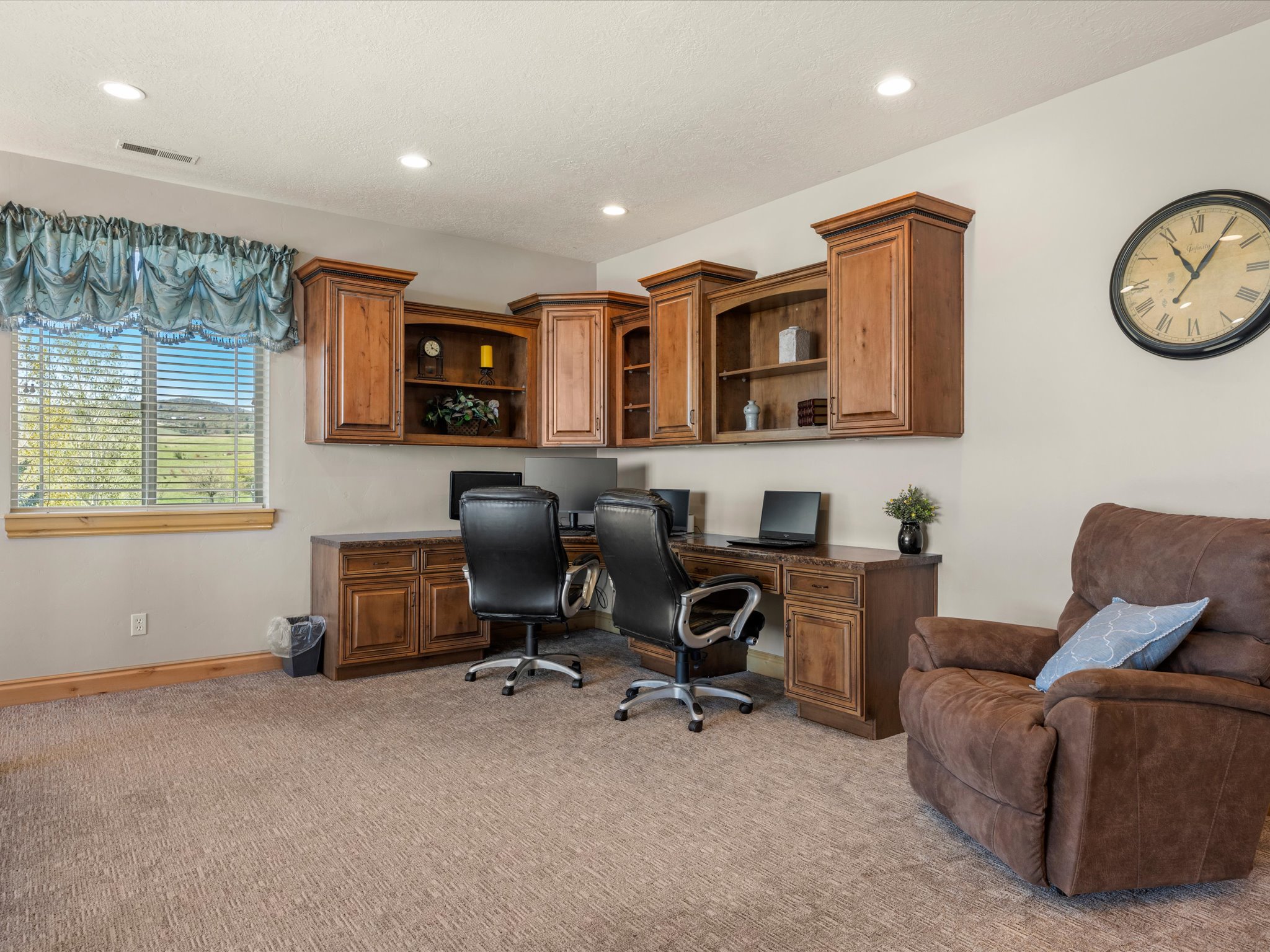 Dedicated workspace featuring extensive built-in cabinetry, dual workstations, recessed lighting, and a large window