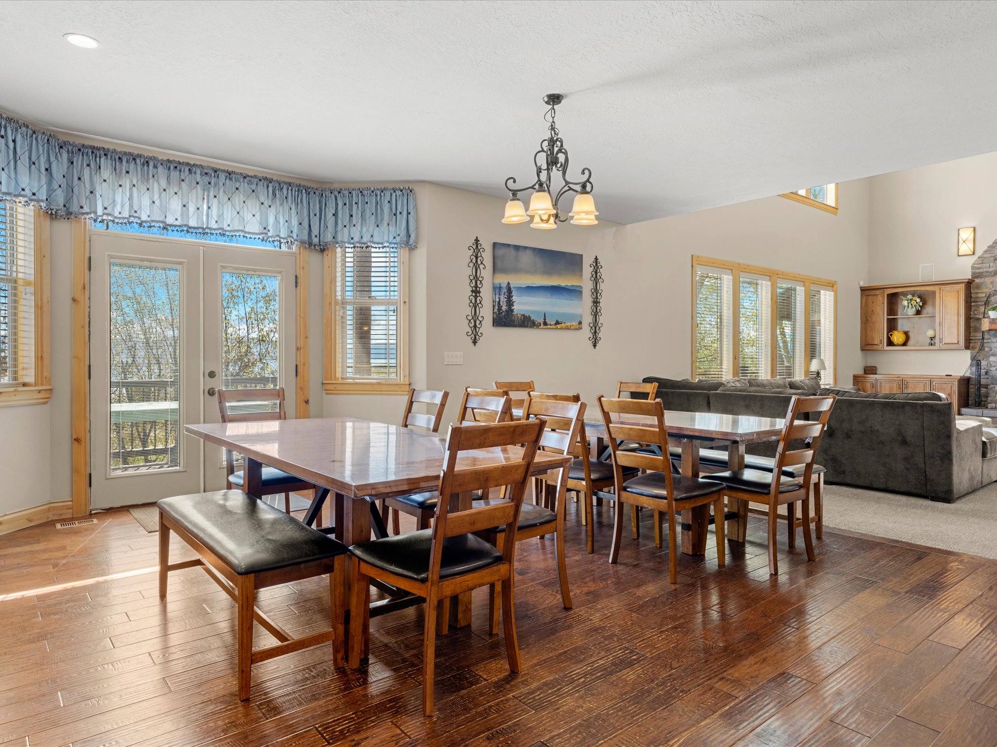 Open-concept dining area featuring wood-finish flooring, a decorative chandelier, and abundant natural light from multiple windows and glass doors