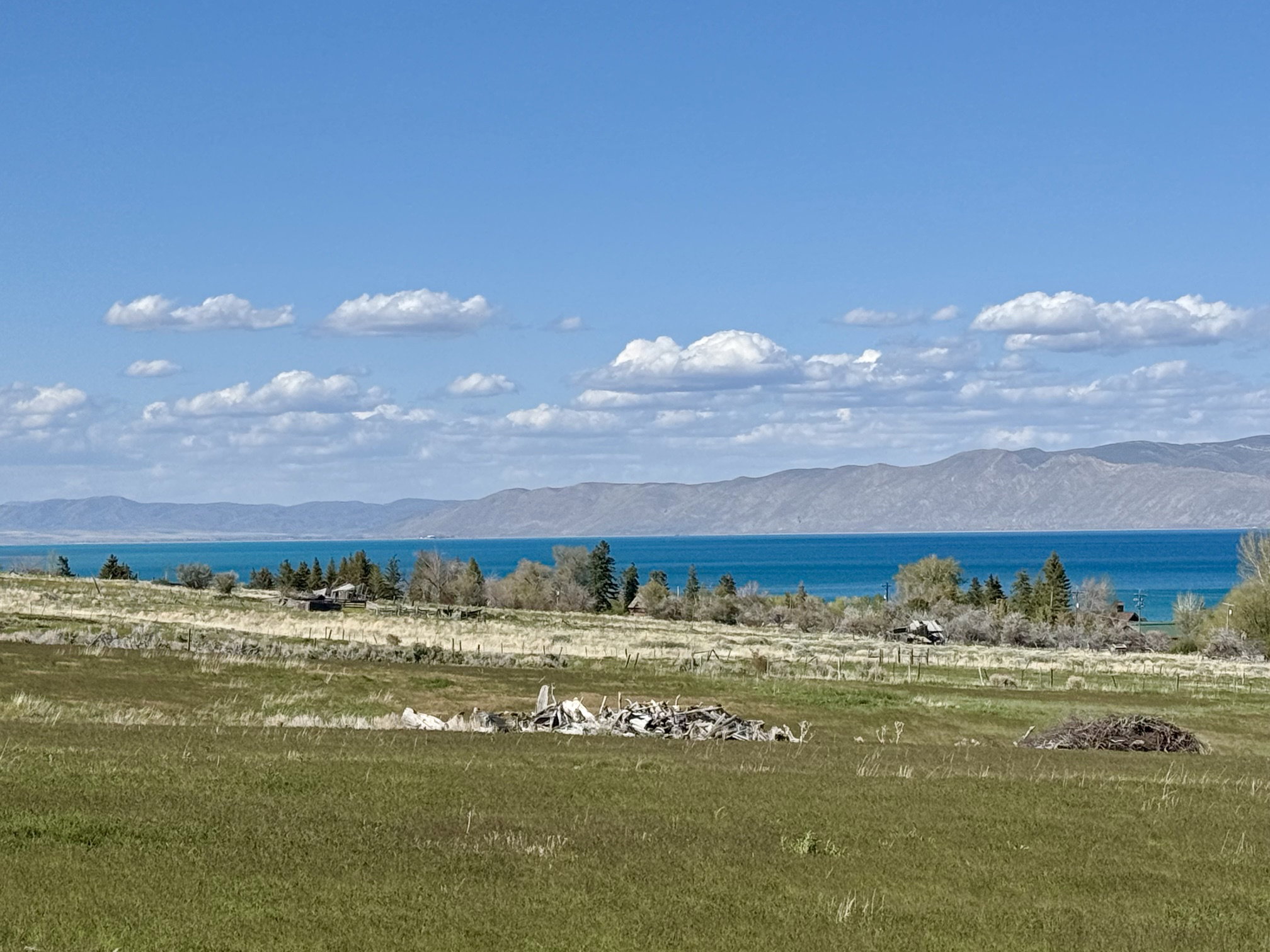 Expansive undeveloped land featuring a broad field, natural foliage, distant mountain ranges, and a large body of water