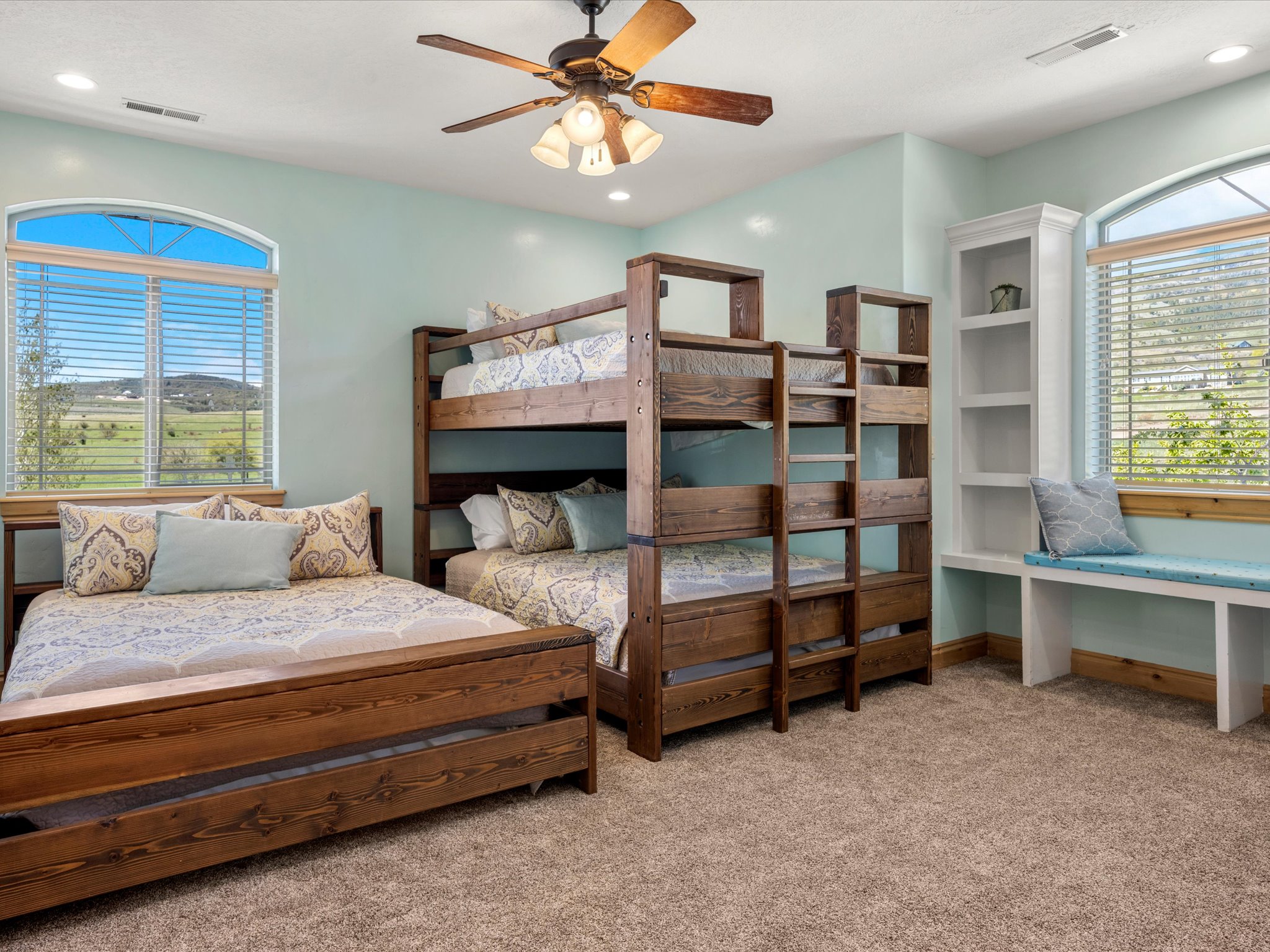 Spacious room featuring multiple beds, a built-in window seat, integrated shelving, and a ceiling fan