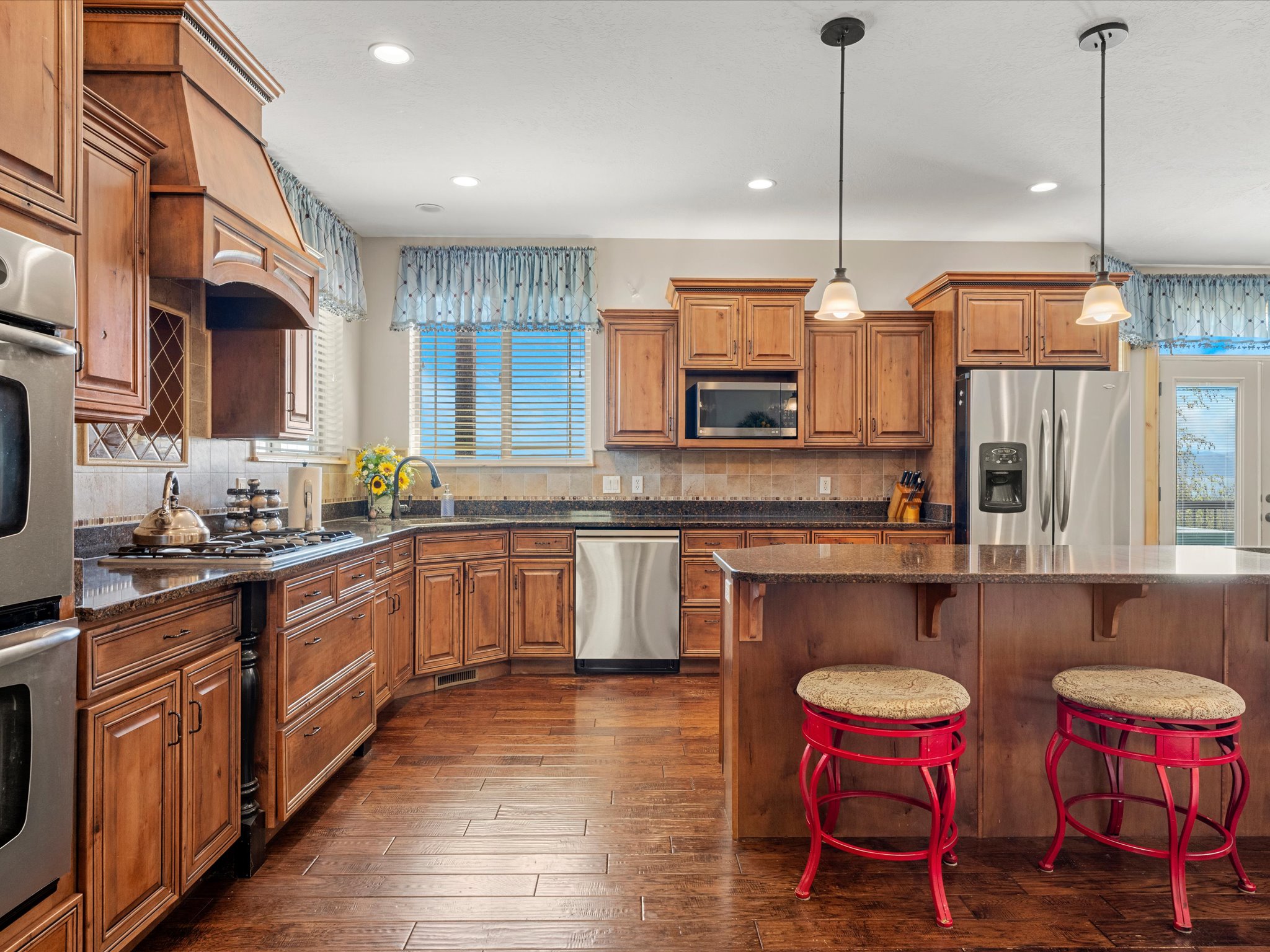Kitchen featuring extensive wood cabinetry, dark countertops, stainless steel appliances, a center island with pendant lighting, and wood-finish flooring