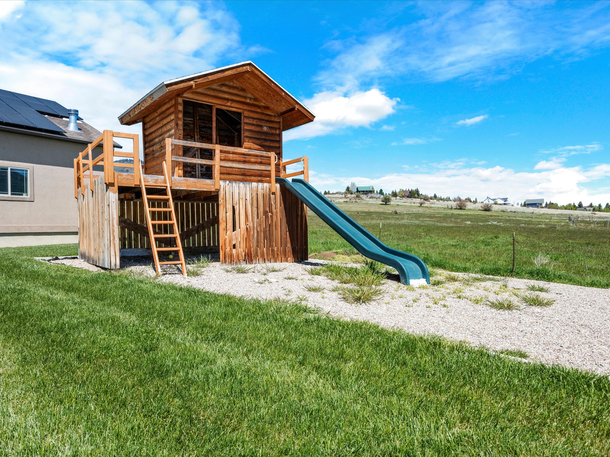 Detached wooden play structure featuring a log cabin design, raised platform, ladder access, and an attached slide