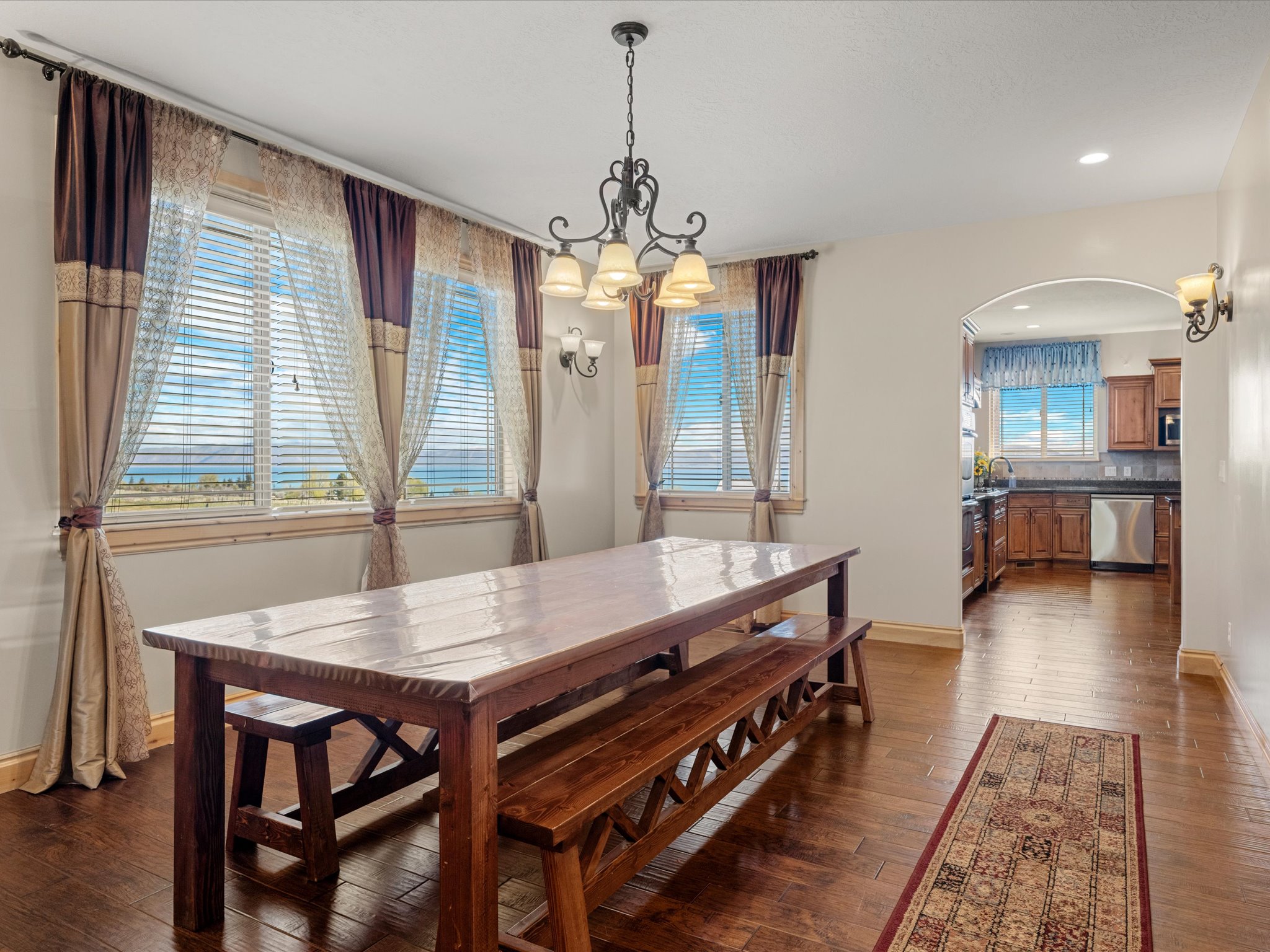 Formal Dining area featuring rich wood-finish flooring, an ornate iron chandelier, and dual windows with horizontal blinds