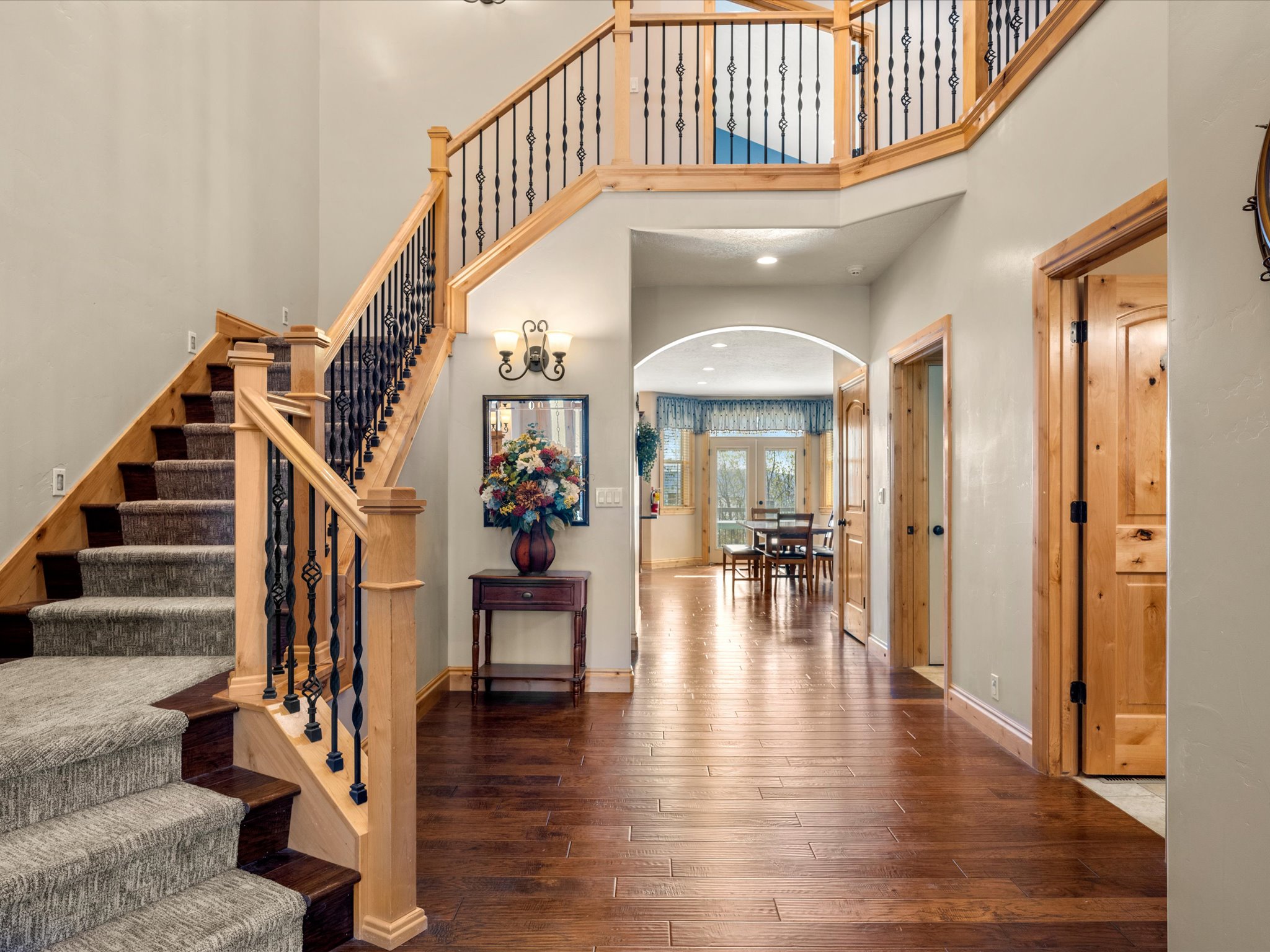 Two-story entryway featuring a grand staircase with wrought iron balusters and natural wood newel posts