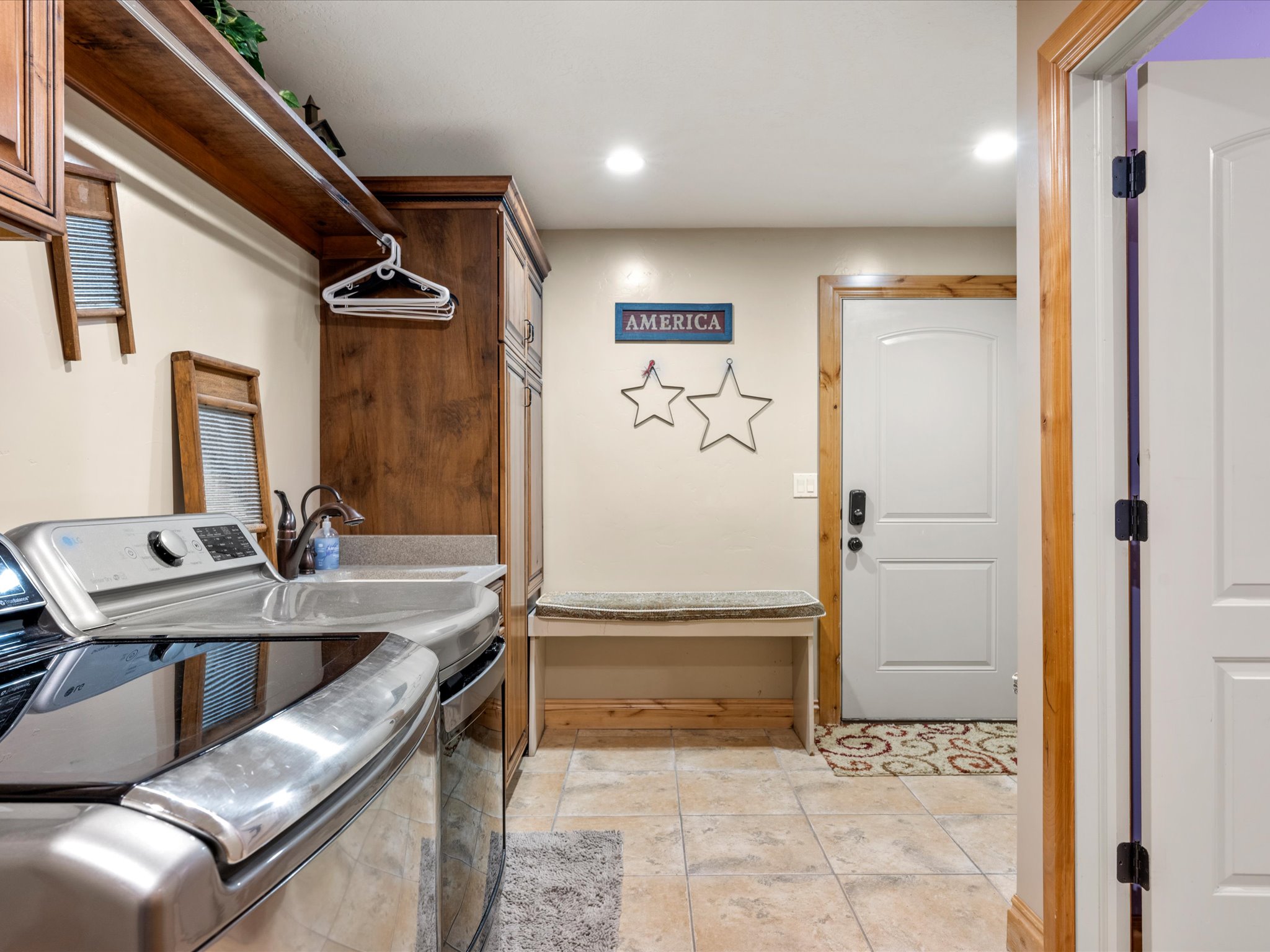 Basement laundry room.Dedicated utility space featuring wood-finish cabinetry, a utility sink with an integrated countertop, recessed lighting, and tile flooring