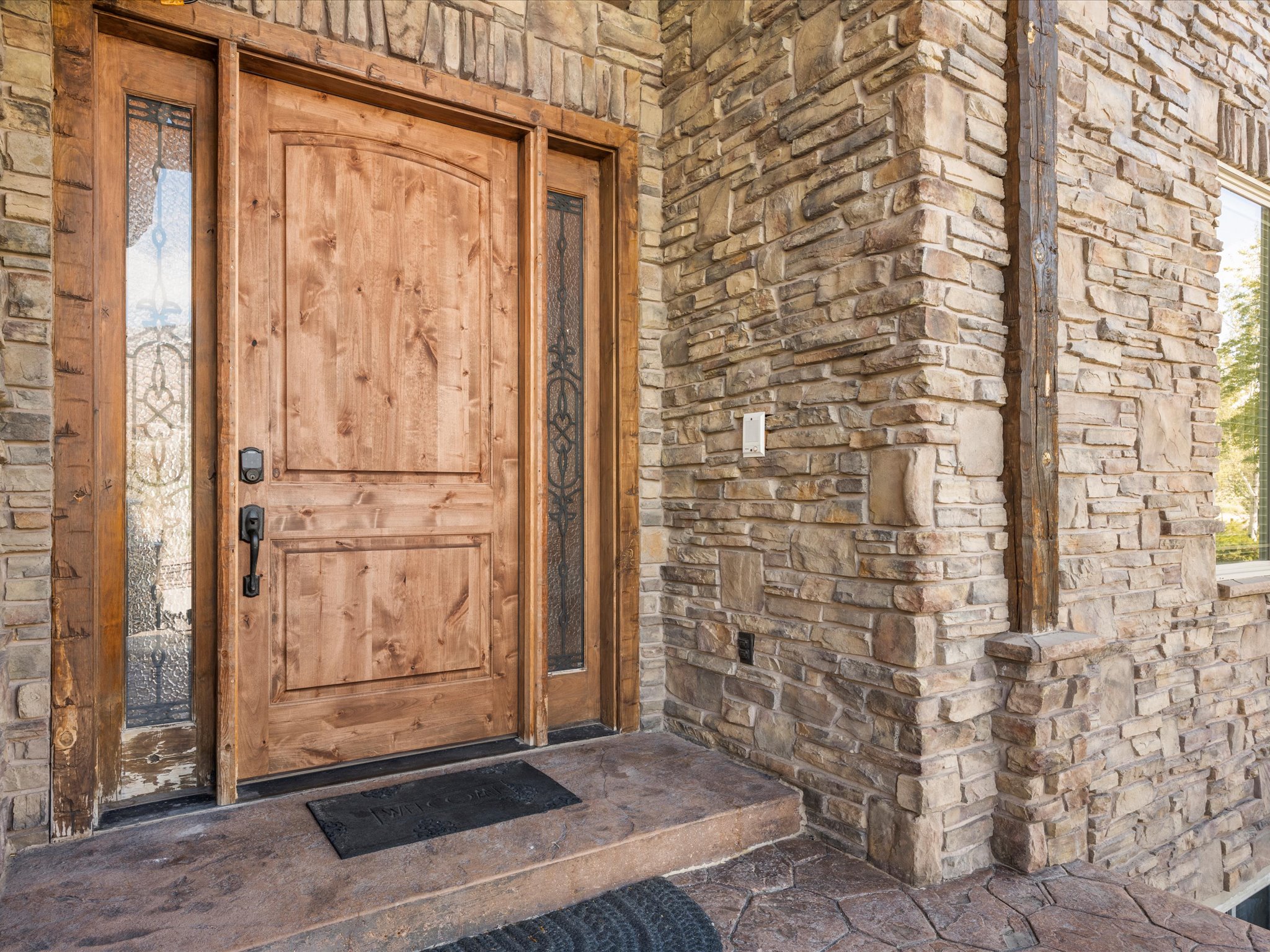 Solid wood entry door with decorative glass sidelights, set within a stone-clad exterior