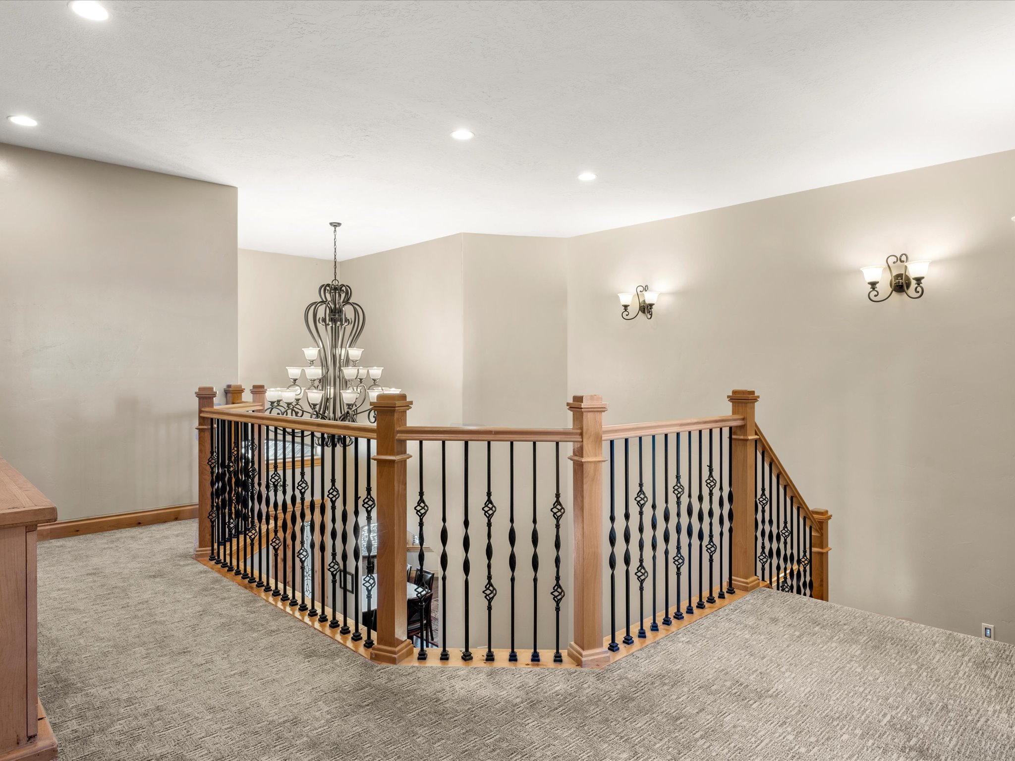 Upper-level landing featuring a wood and wrought iron railing, recessed lighting, and wall-mounted sconces