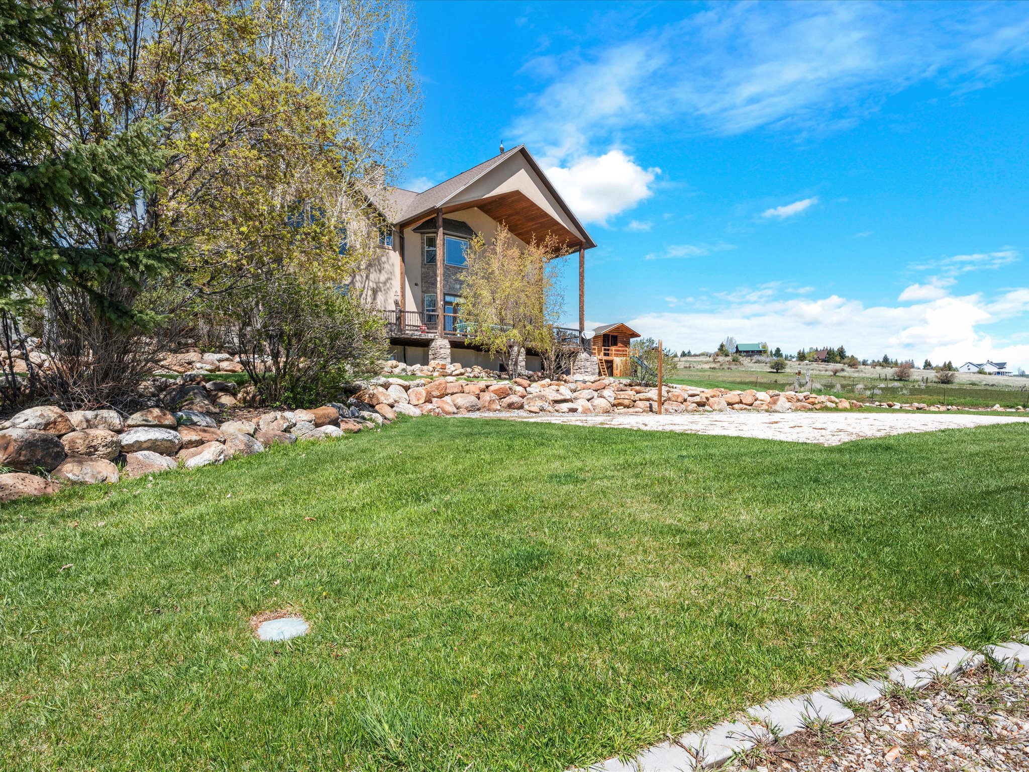 Expansive lawn with a decorative rock wall, mature landscaping, and a multi-level deck